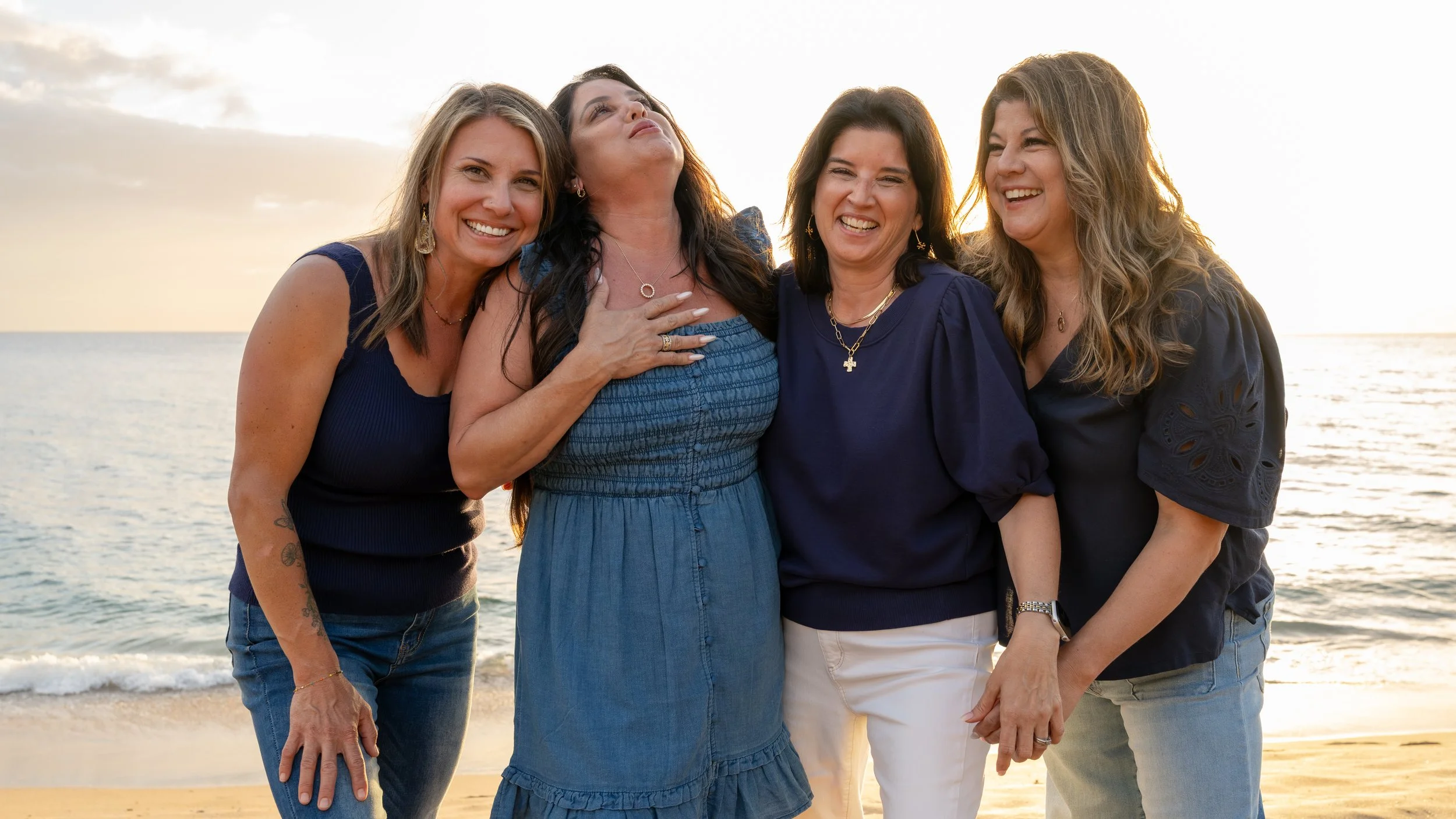 Four sisters sharing a laugh on a Maui beach at sunset during a family portrait session.