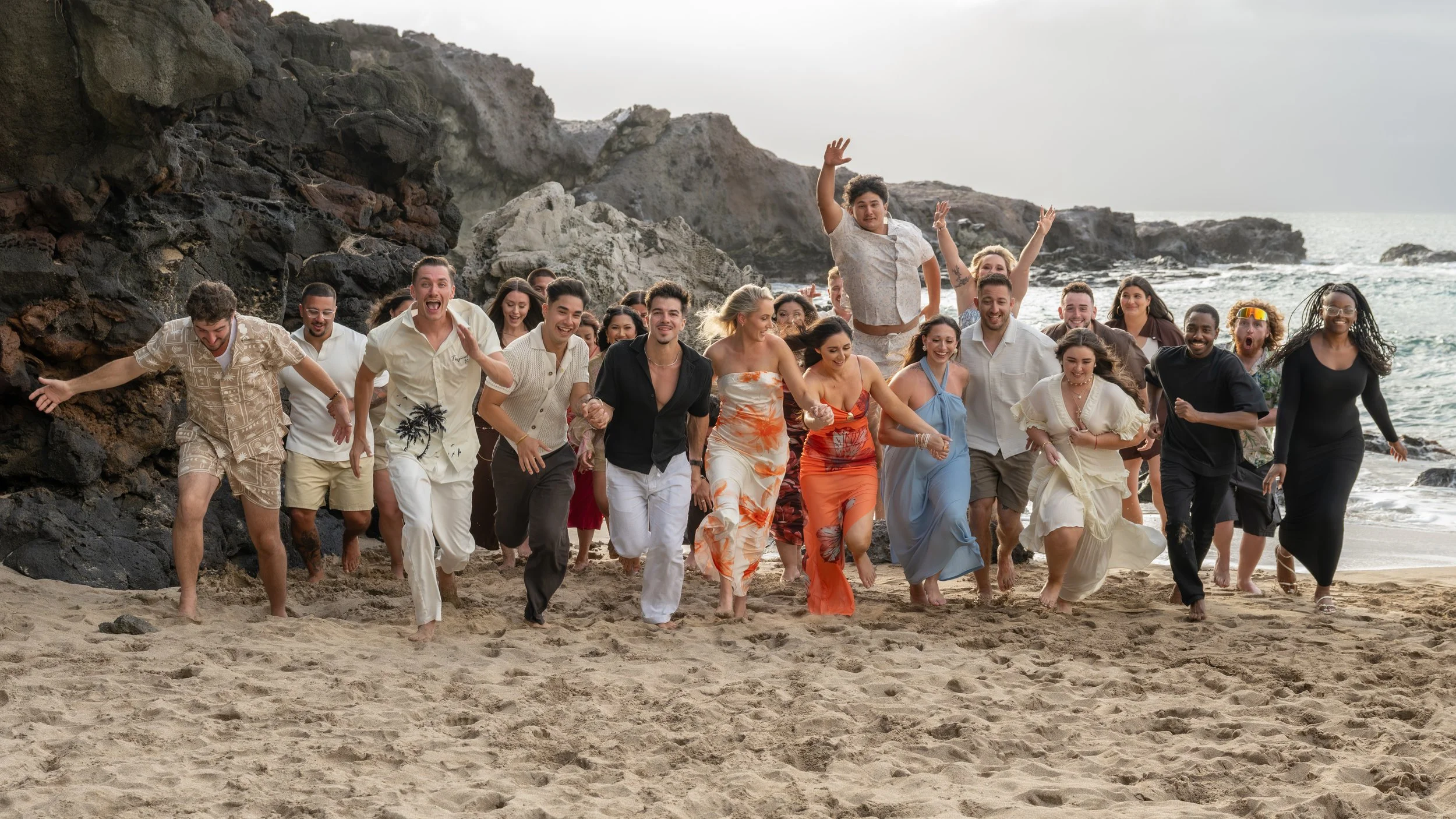 Family and friends laughing and running together on a Maui beach beside lava rock formations.