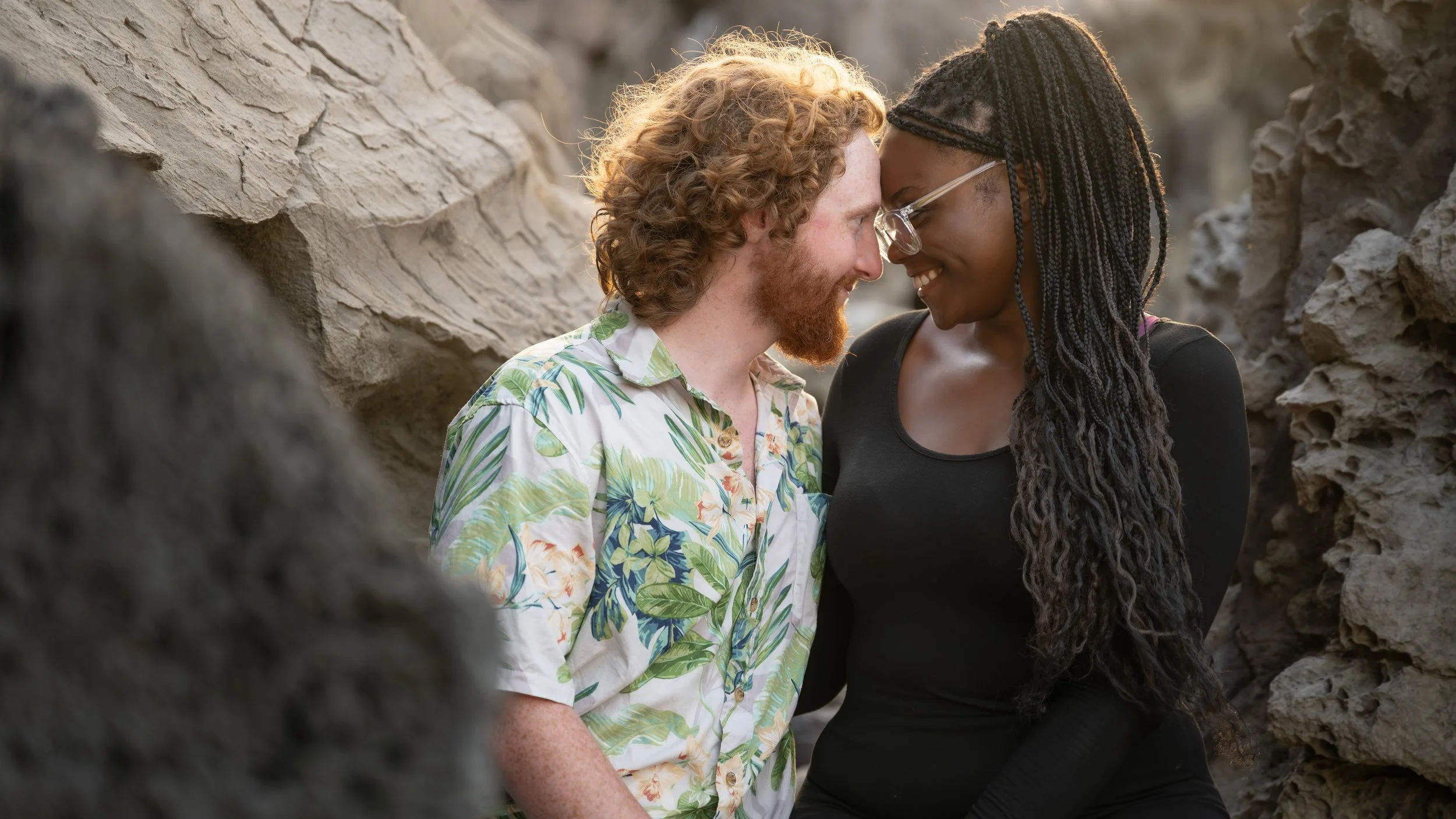 Couple smiling with their foreheads touching, framed by lava rocks on a Maui beach.