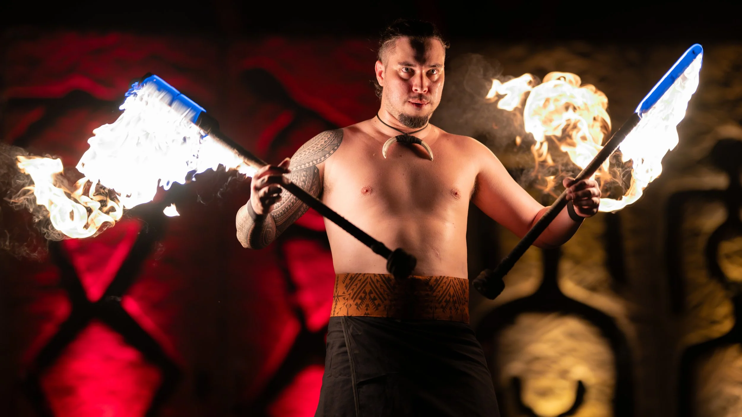 Samoan fire knife dancer performing with two flaming knives on a dramatically lit stage.