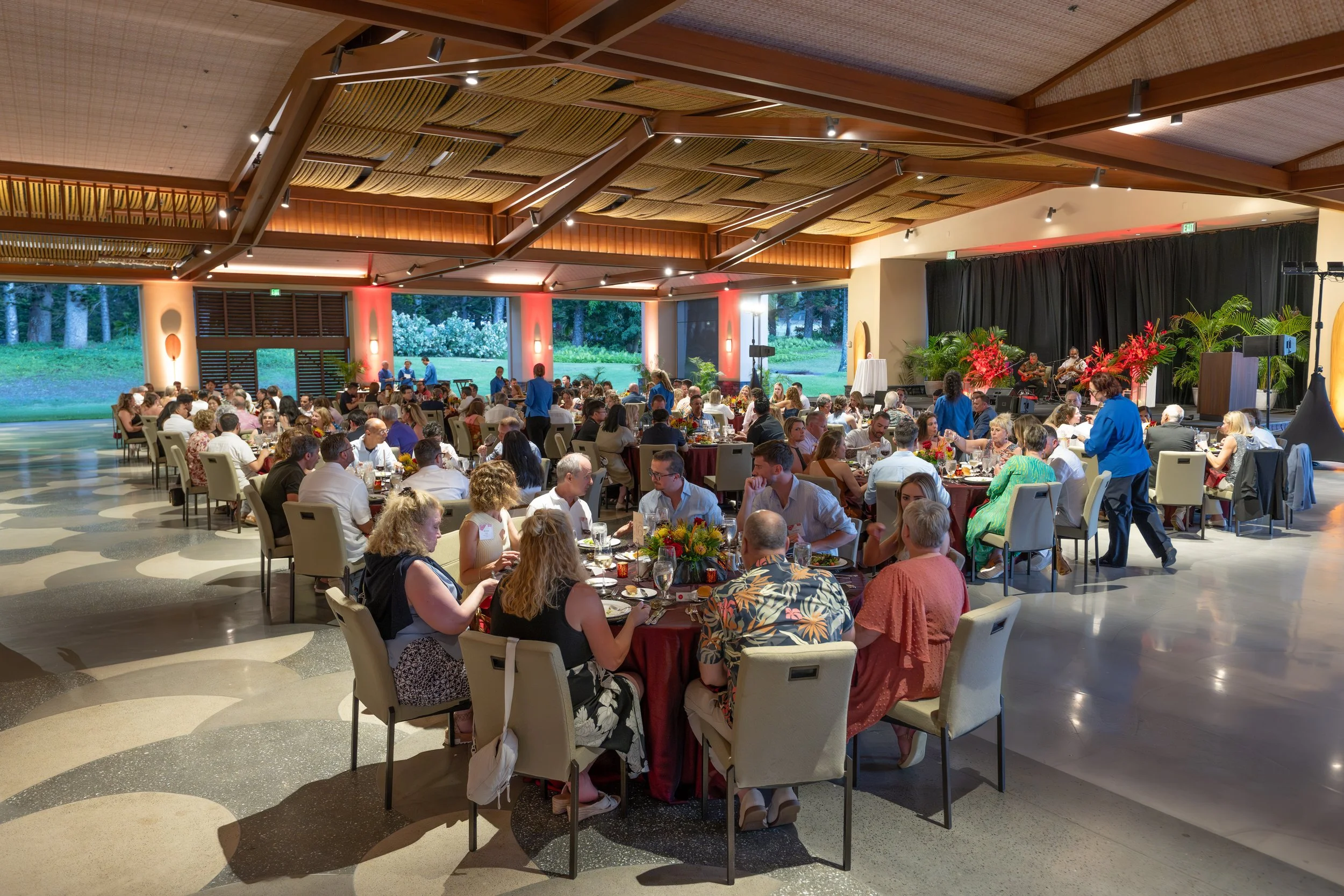 Guests seated at round tables during a corporate dinner in a Maui ballroom with exposed wooden beams.