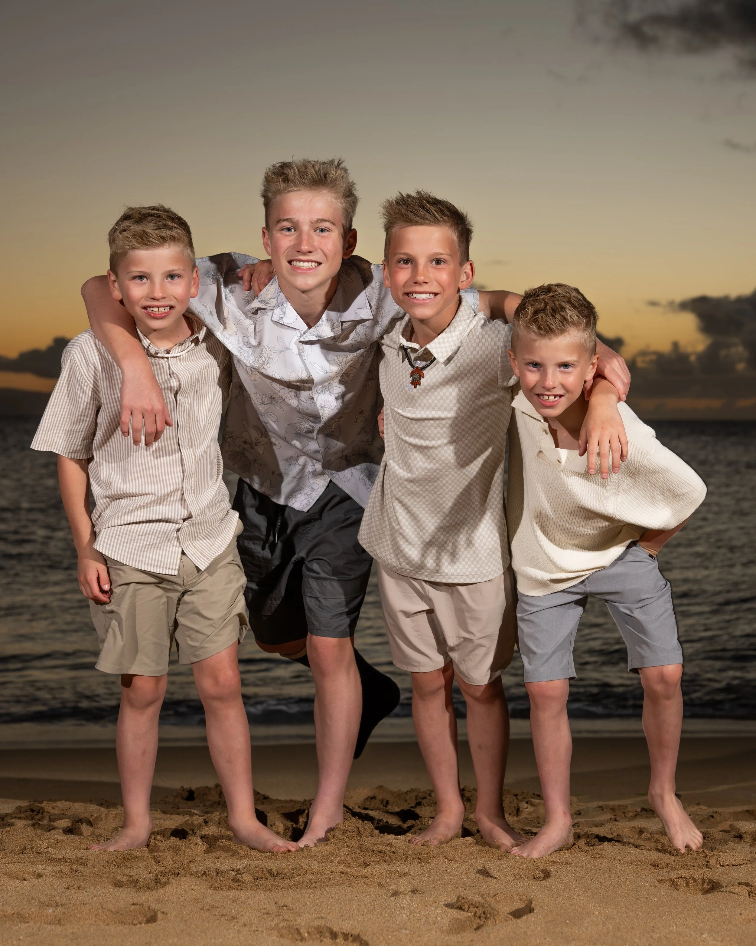 Four brothers smiling with their arms around one another on a Maui beach at sunset.
