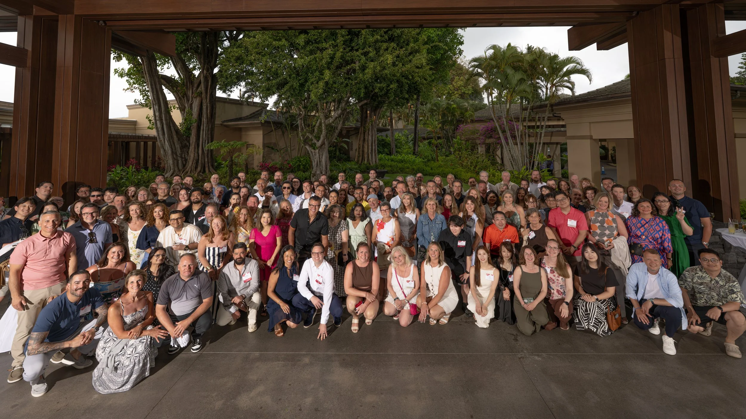 Corporate attendees gathered for a large group portrait beneath a wooden pavilion.