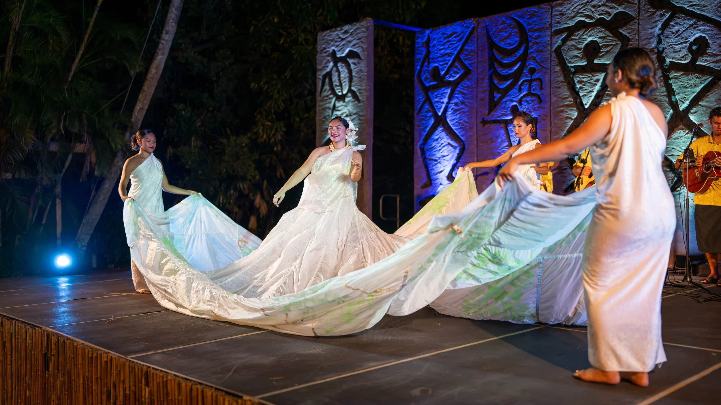 Dancers swirling flowing white skirts across a stage with blue lighting.