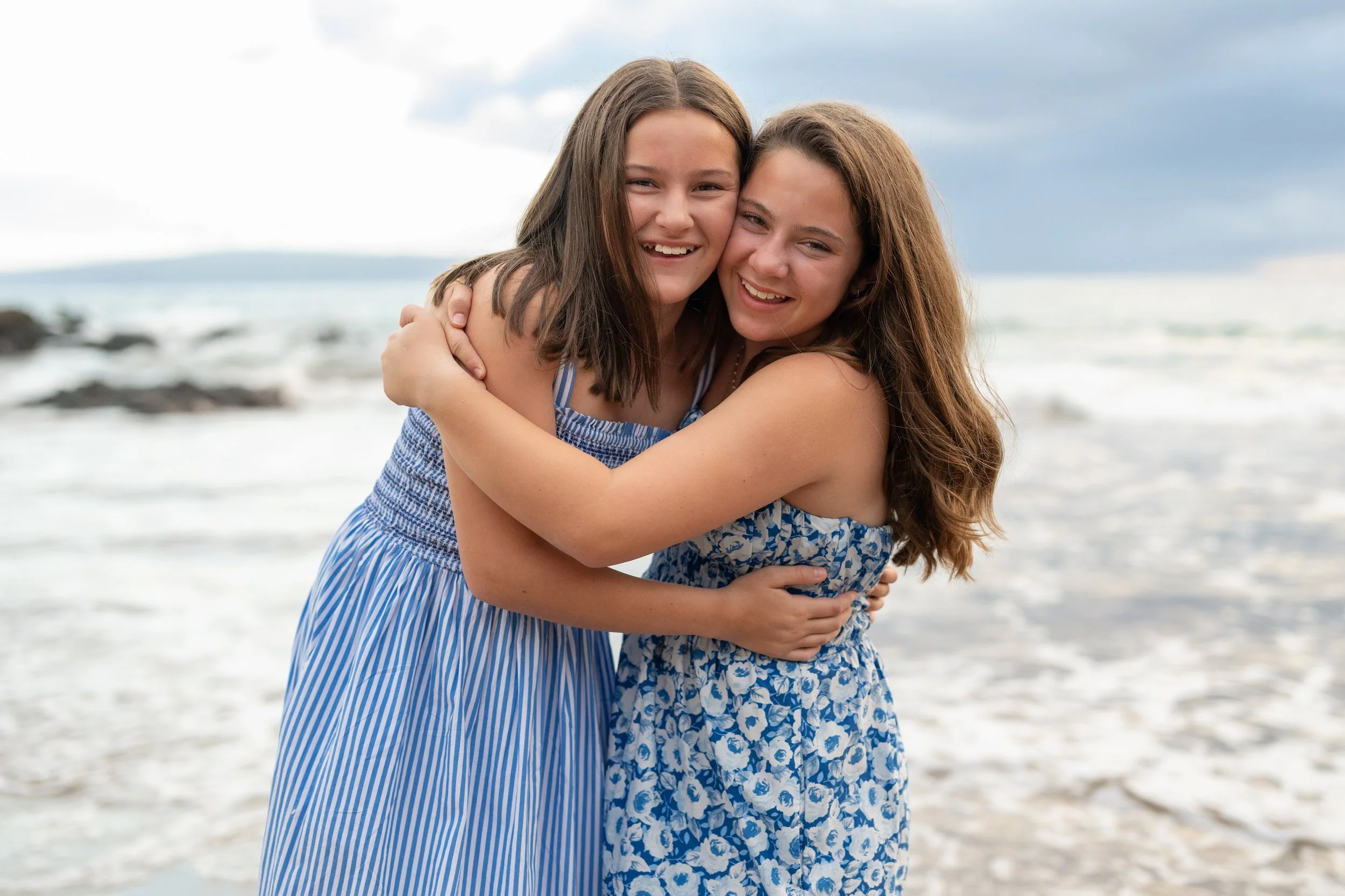 Two smiling cousins embracing on a Maui beach.