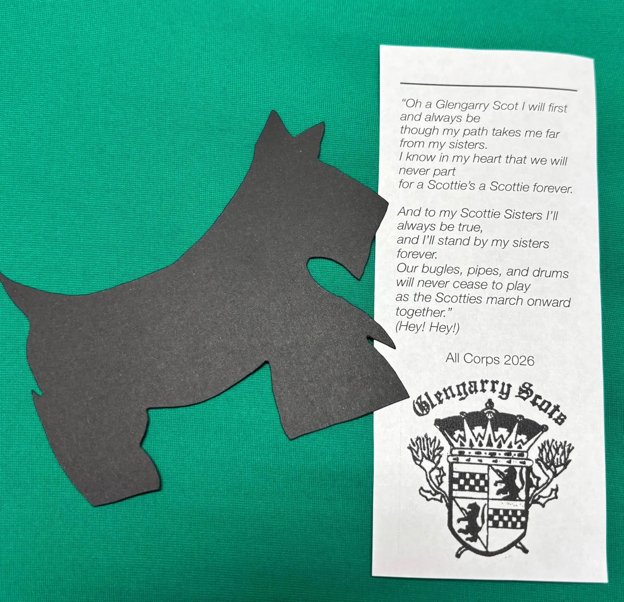 A black silhouette of a dog's head with a pointed ear, partially visible under a green background, alongside a white paper with printed text and a crest or emblem containing a coat of arms.