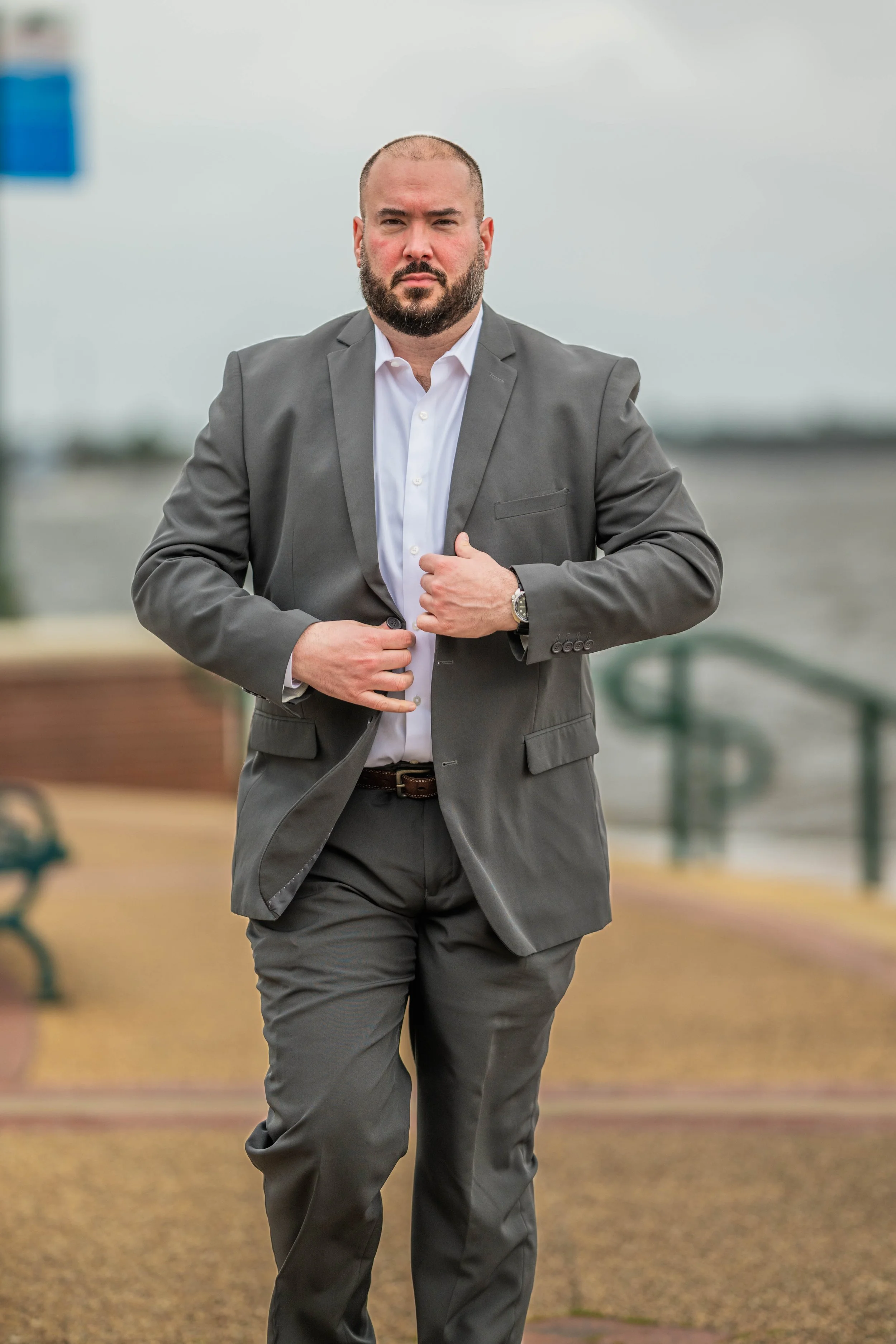 Man in a gray suit walking outdoors near water