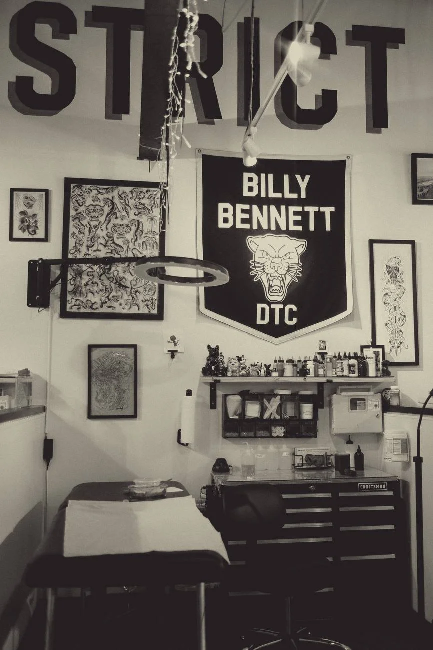 A tattoo station under Billy Bennett's panther pennant, with framed flash on the wall