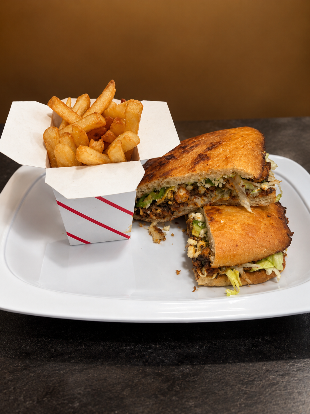 Fried chicken sandwich with lettuce and sauce, served with a side of French fries in a paper container, on a white plate