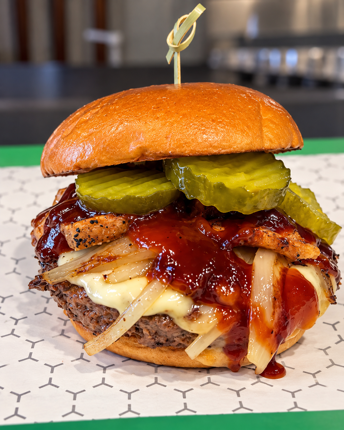 Close-up of a burger with pickles, melted cheese, grilled chicken, barbecue sauce, and a toasted bun, topped with a skewer.