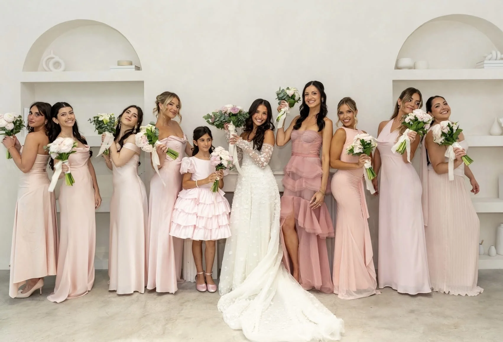 Bride, flower girl, and bridesmaids in pink dresses pose with bouquets at a wedding.