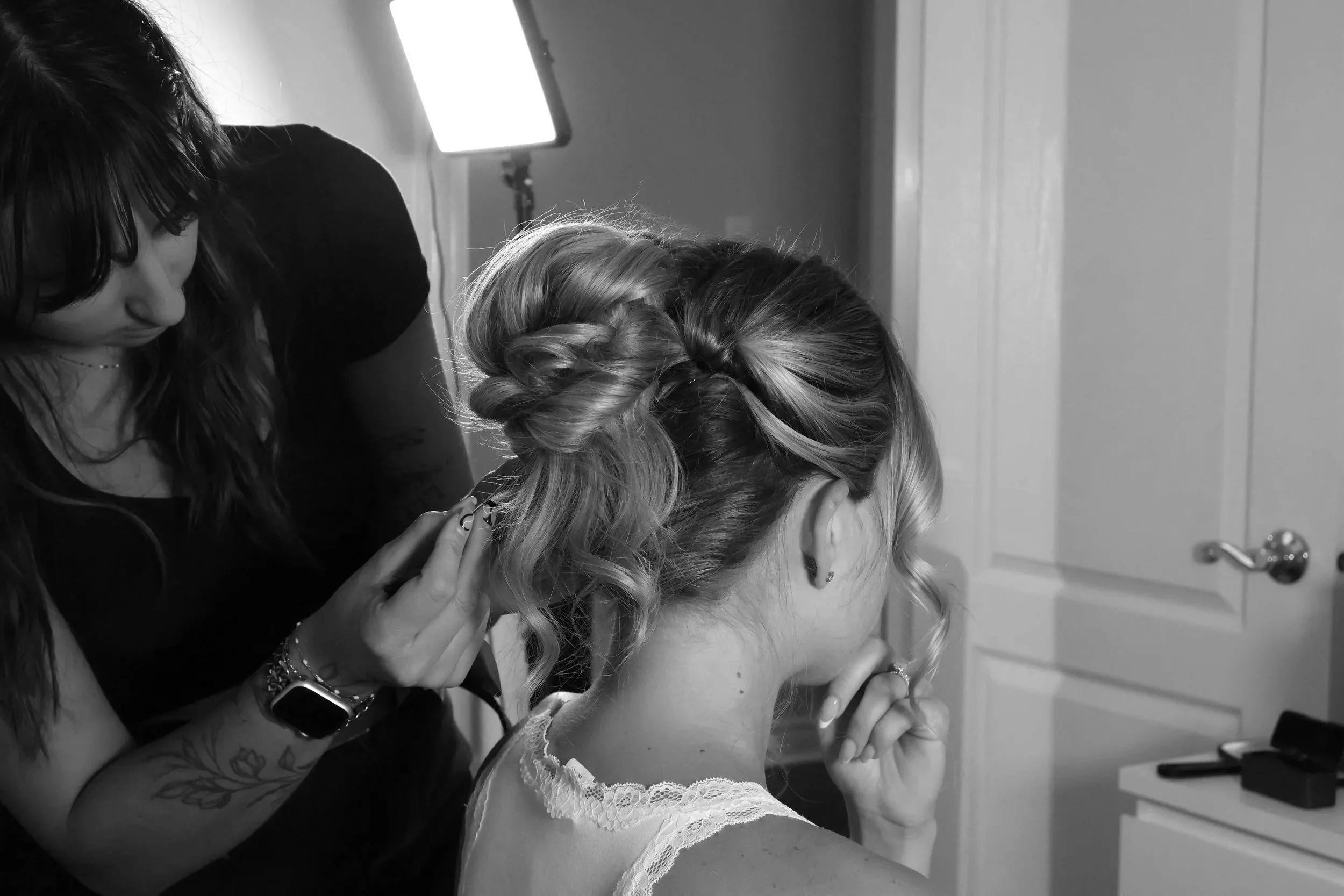 Hairstylist pinning an elegant updo on a bride wearing a lace dress