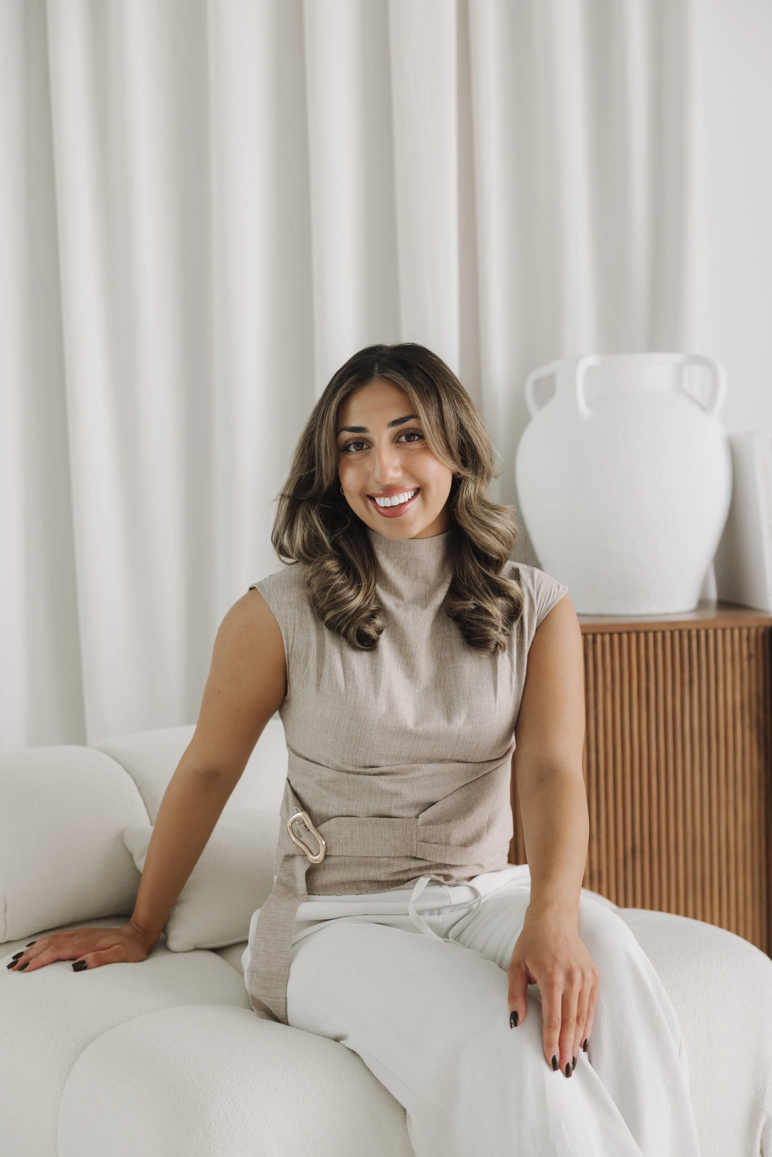 Smiling woman with long wavy hair sitting on a white couch in a bright living room