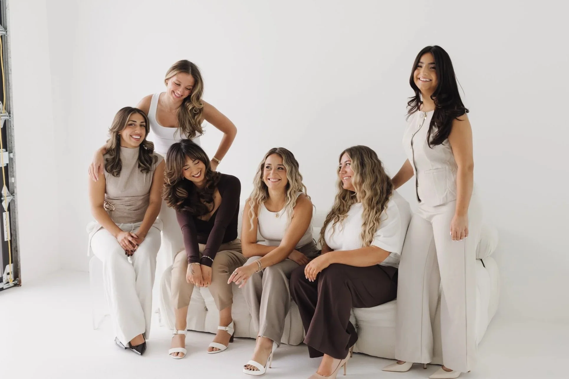 Group of six smiling women posing together in a bright white studio