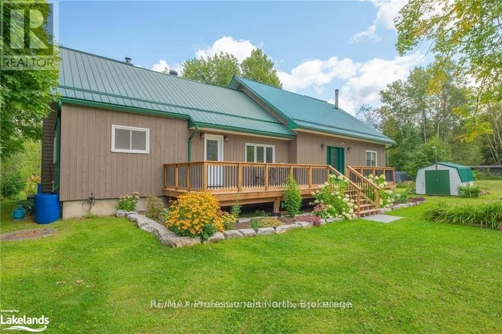 Exterior of 1026 Dewey Street in Highlands East, Ontario, featuring a rural home with a green metal roof, wooden deck and landscaped yard.