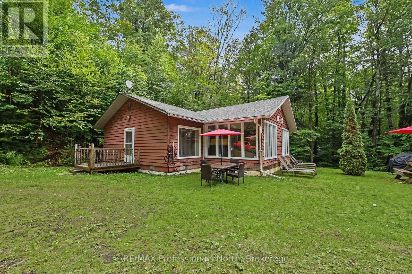 Wood-sided cottage at 1363 Ross Lake Road in Dysart et al, Ontario, featuring a screened porch and outdoor seating surrounded by trees.