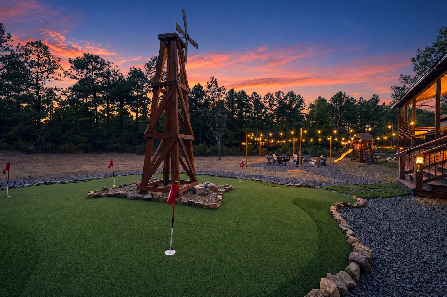 A miniature golf course at dusk with a windmill, small flags, and string lights in the background.