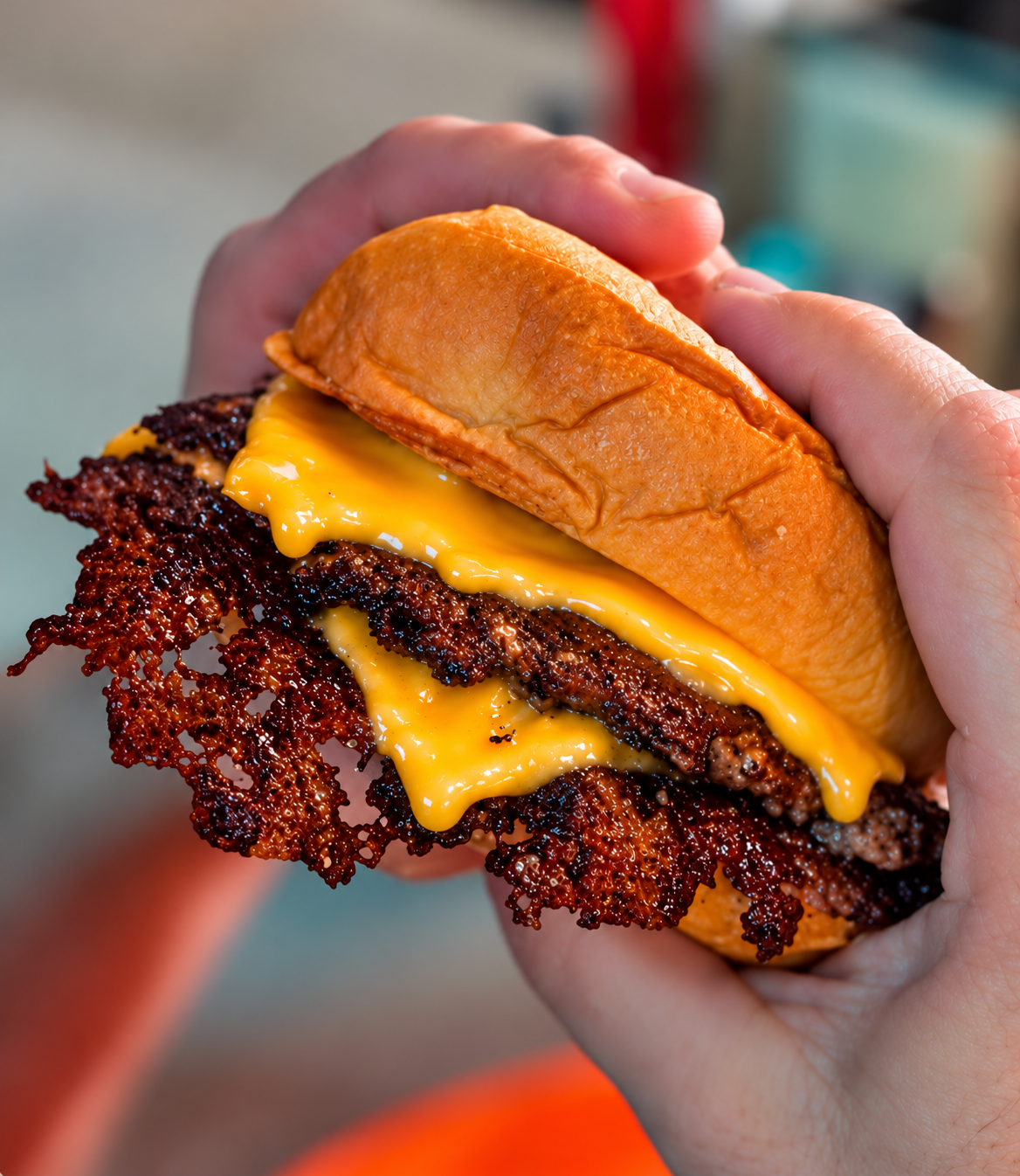 Close-up of a person holding a cheeseburger with crispy bacon, melted cheese, and a sandwich bun.