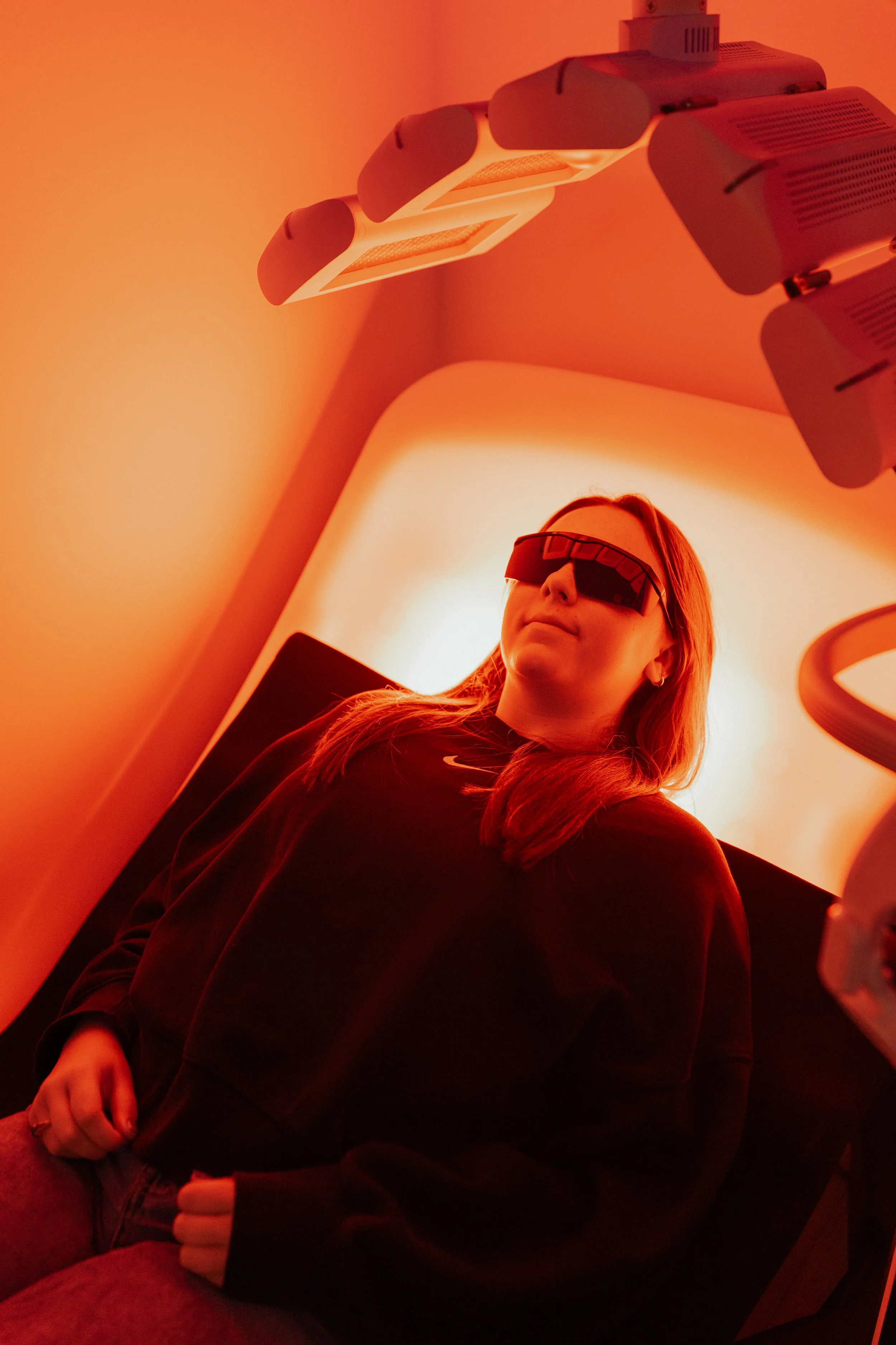 Woman wearing protective goggles lying under red light therapy equipment