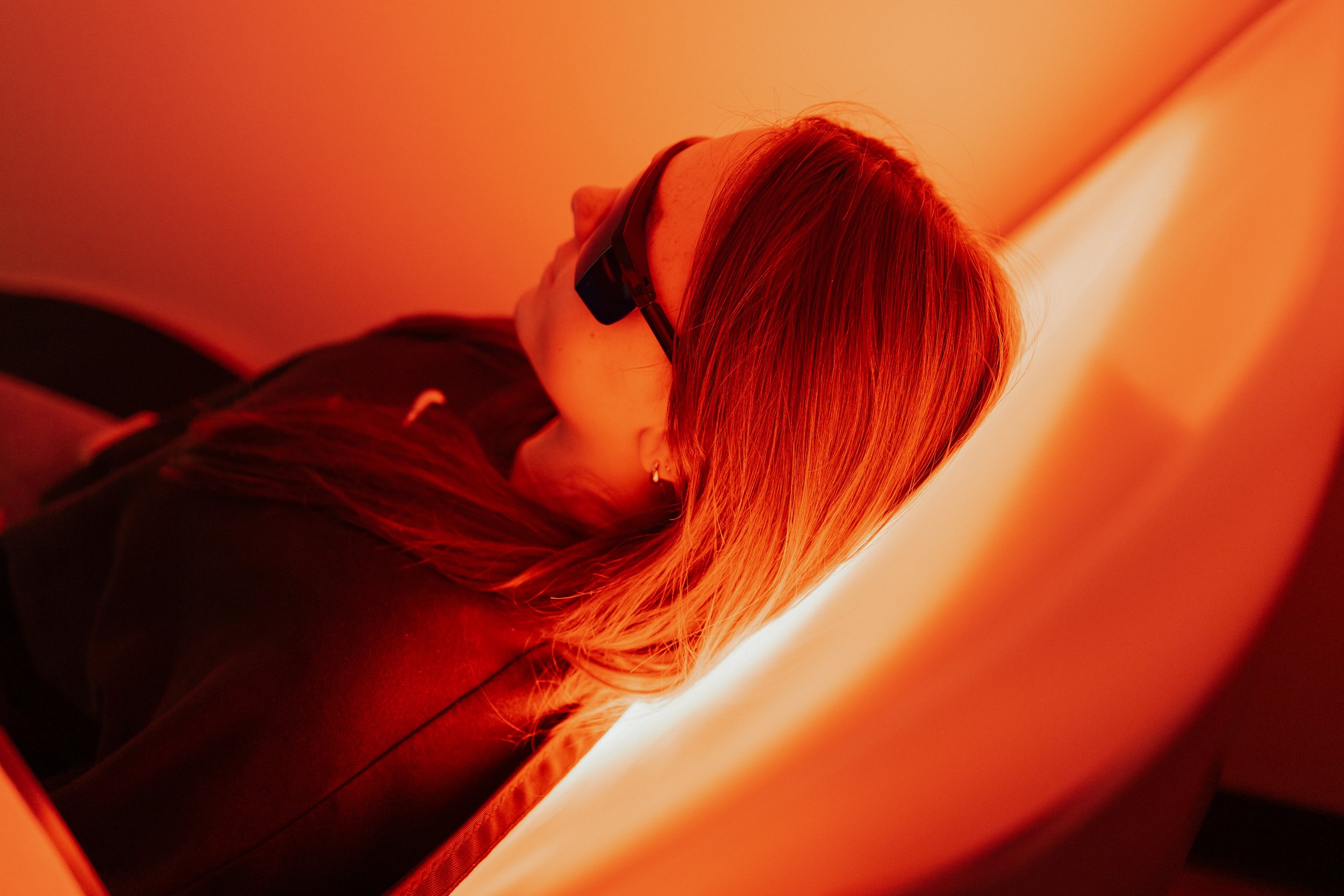Woman with red hair wearing sunglasses, photographed in warm orange light