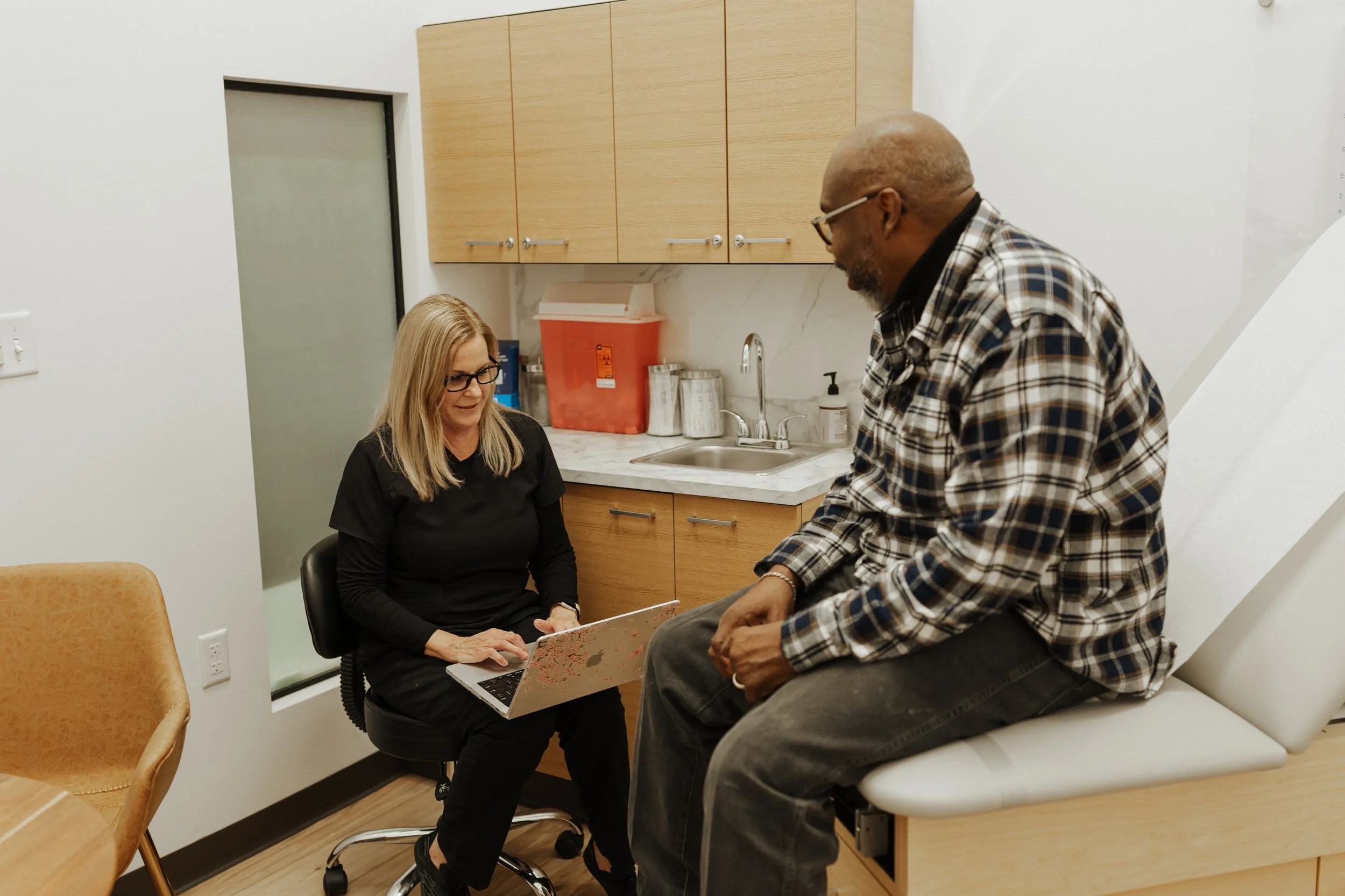 Healthcare professional discussing information with a seated male patient in a medical examination room