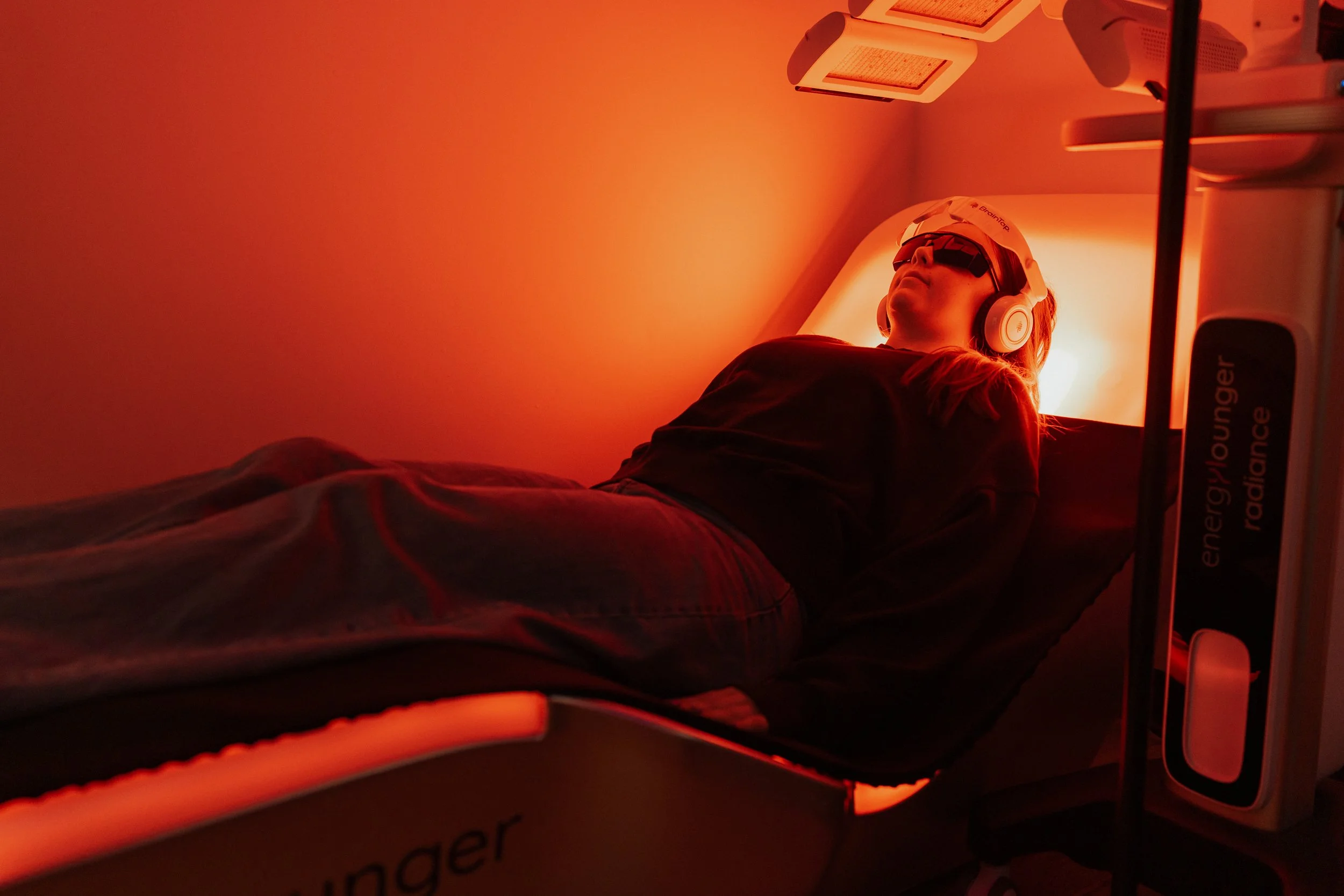 Person wearing protective goggles and headphones lying under red light therapy panels
