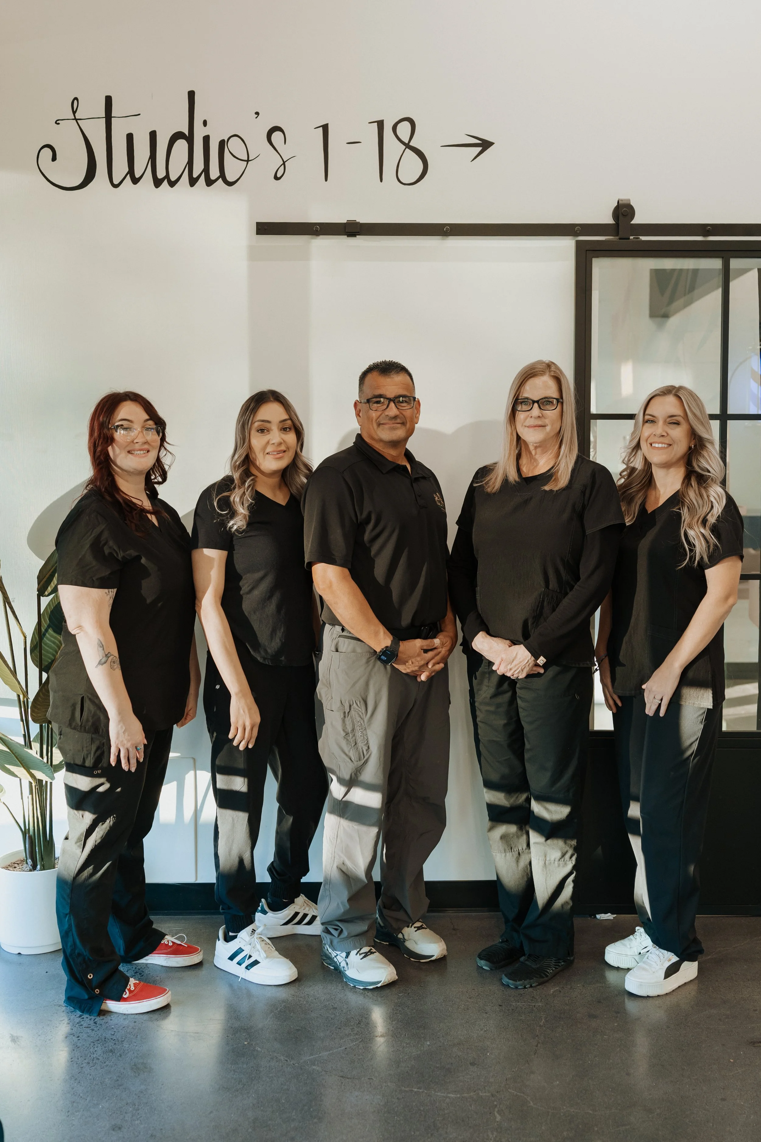 Five-person salon team posing in black uniforms beneath a “Judit’s Salon” sign.