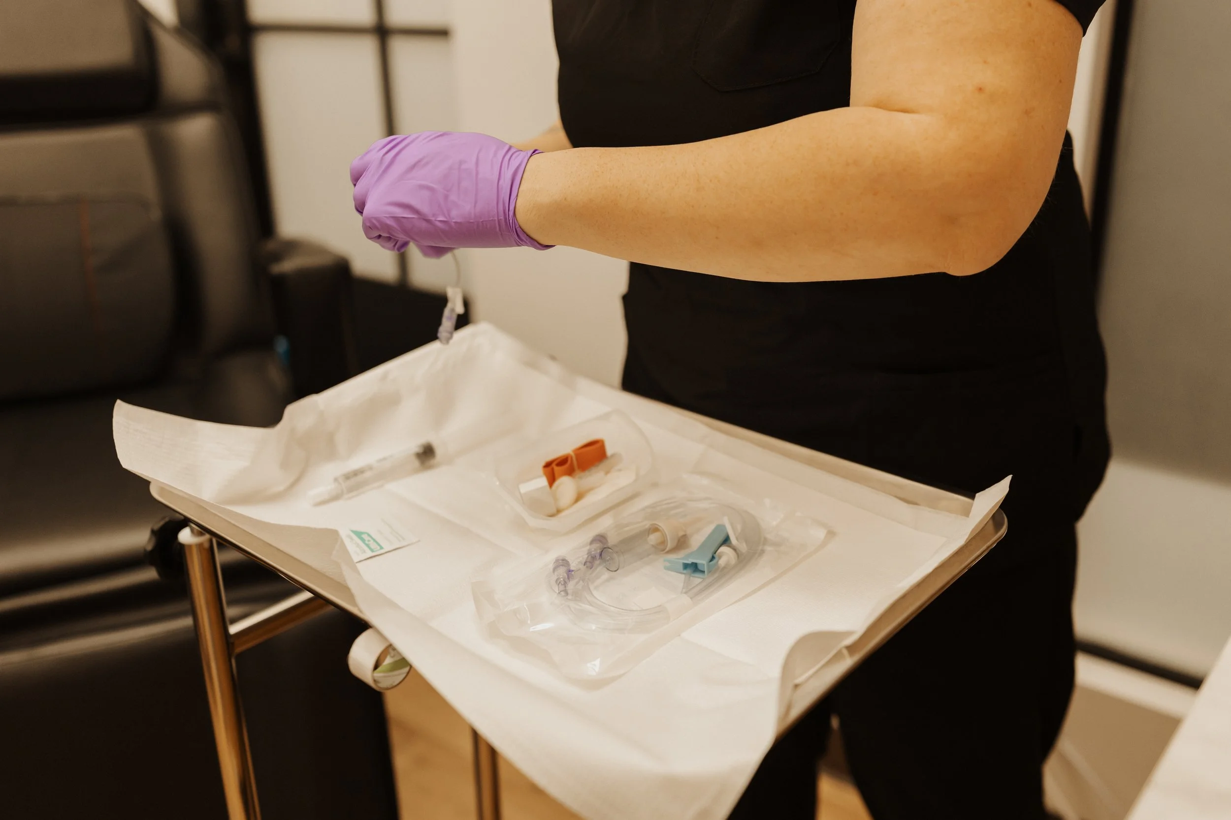 Healthcare worker wearing purple gloves prepares sterile medical supplies and a syringe on a procedure tray.