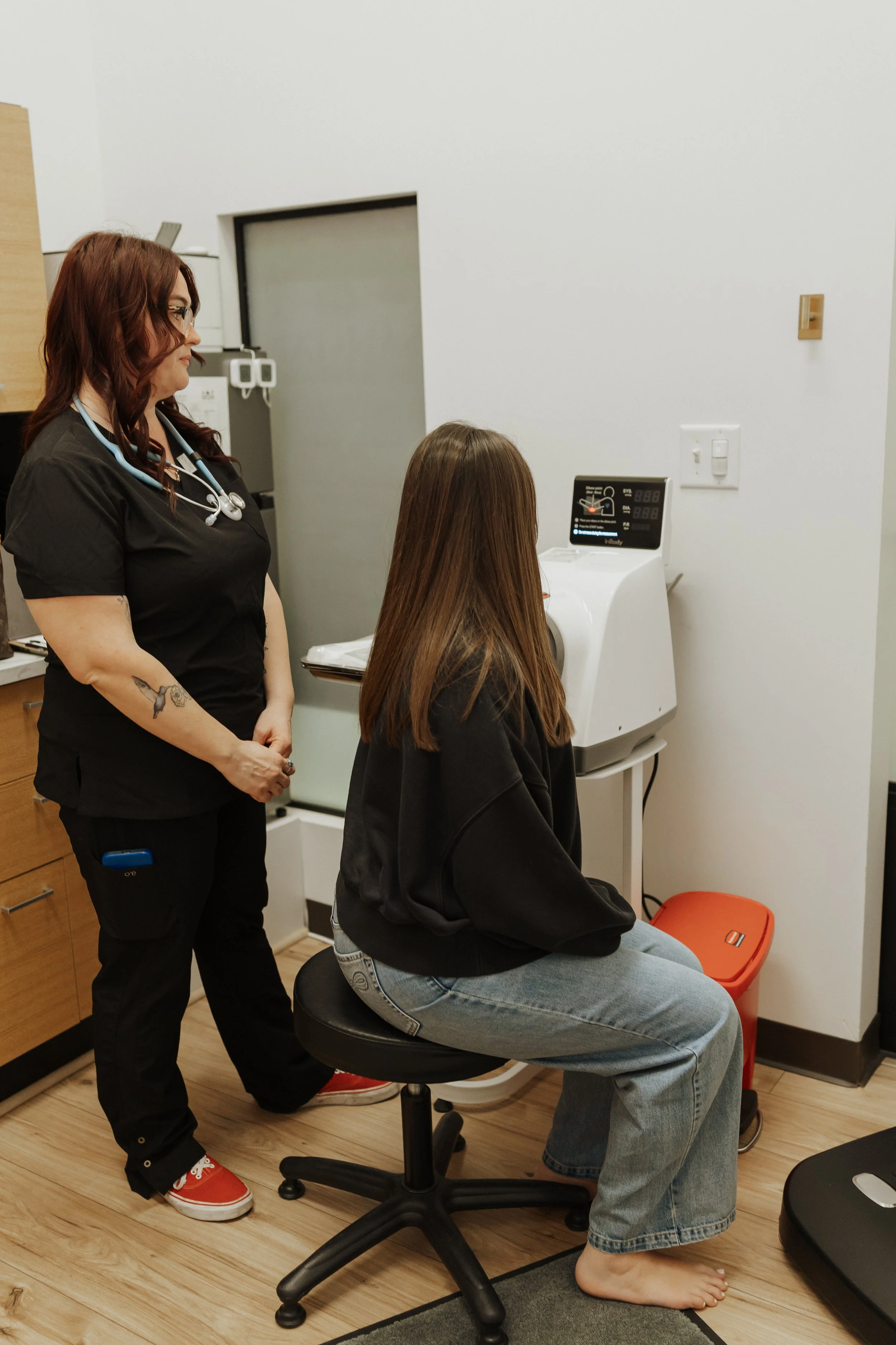 Healthcare professional with a stethoscope attending to a seated patient in a medical examination room.