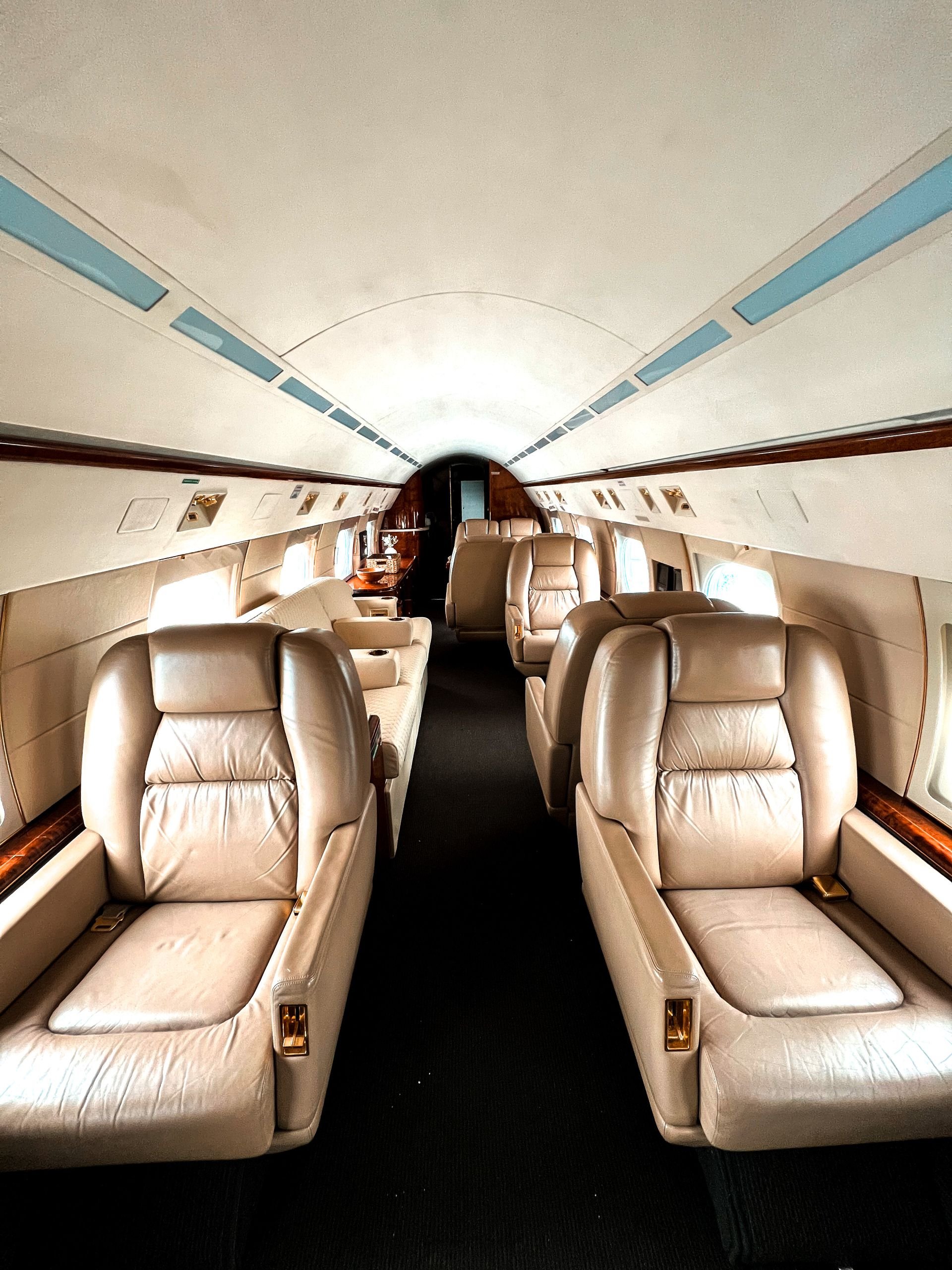 Luxurious private jet cabin with cream leather seats, wood trim, and a central aisle