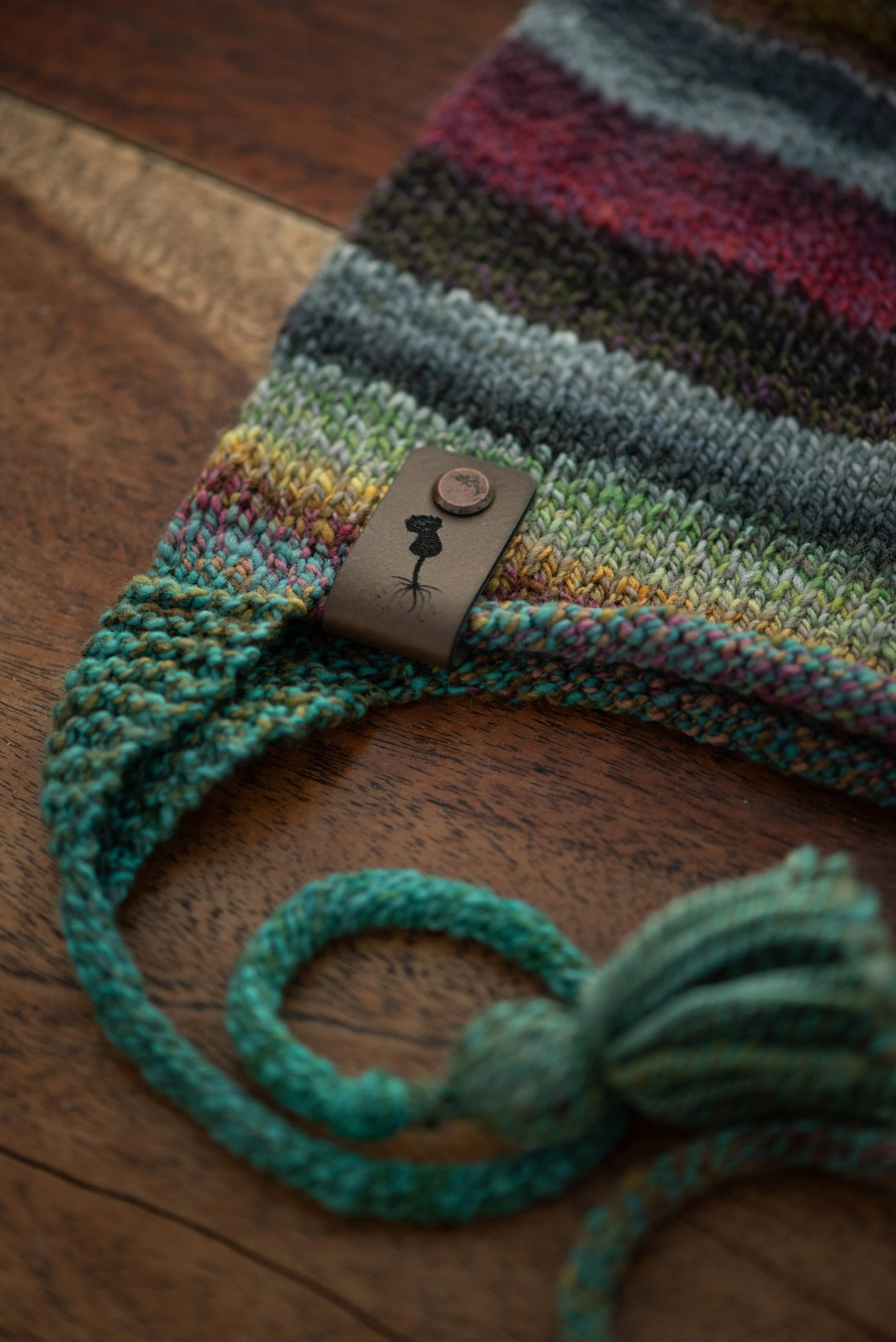 Striped Hudson Hat on a wooden table, with a thistle label, knitted tie and handmade tassel.