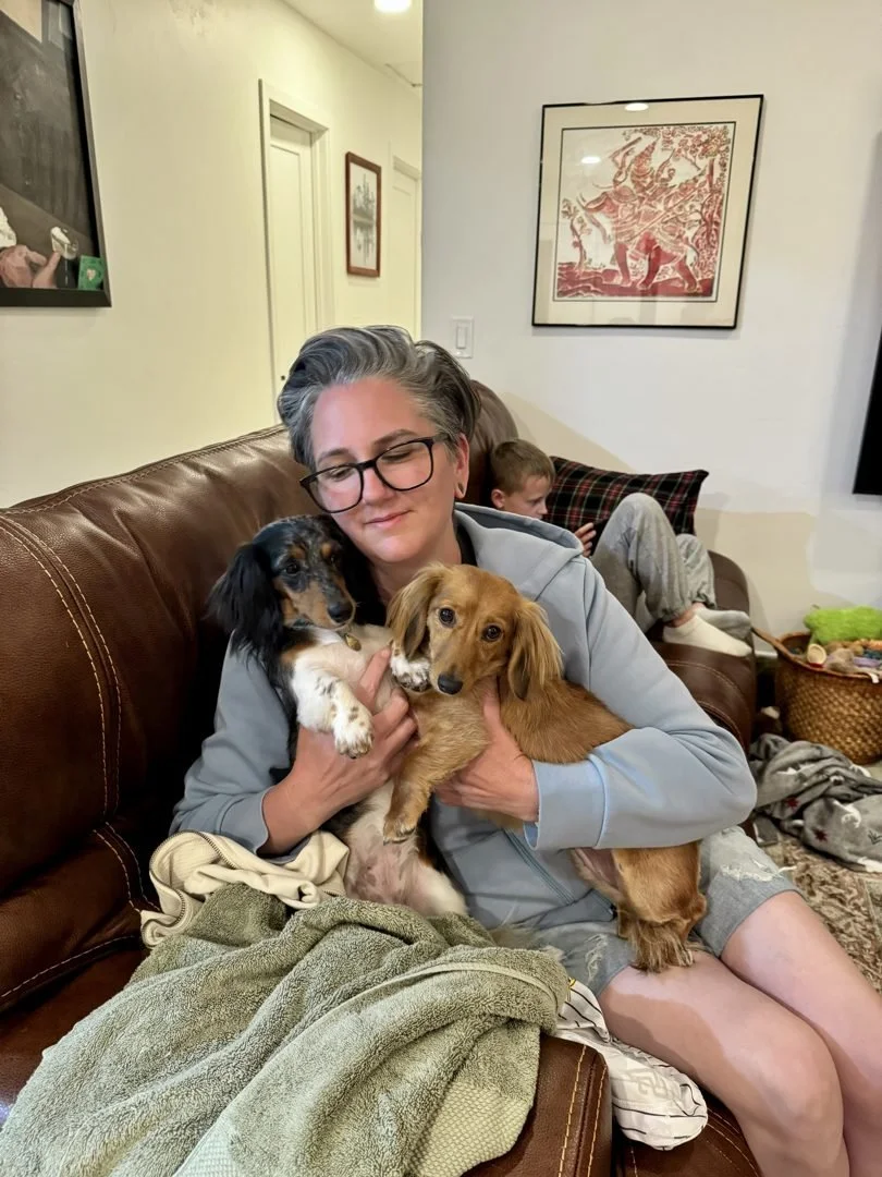 Lindsay sitting on a sofa, holding two dogs close.