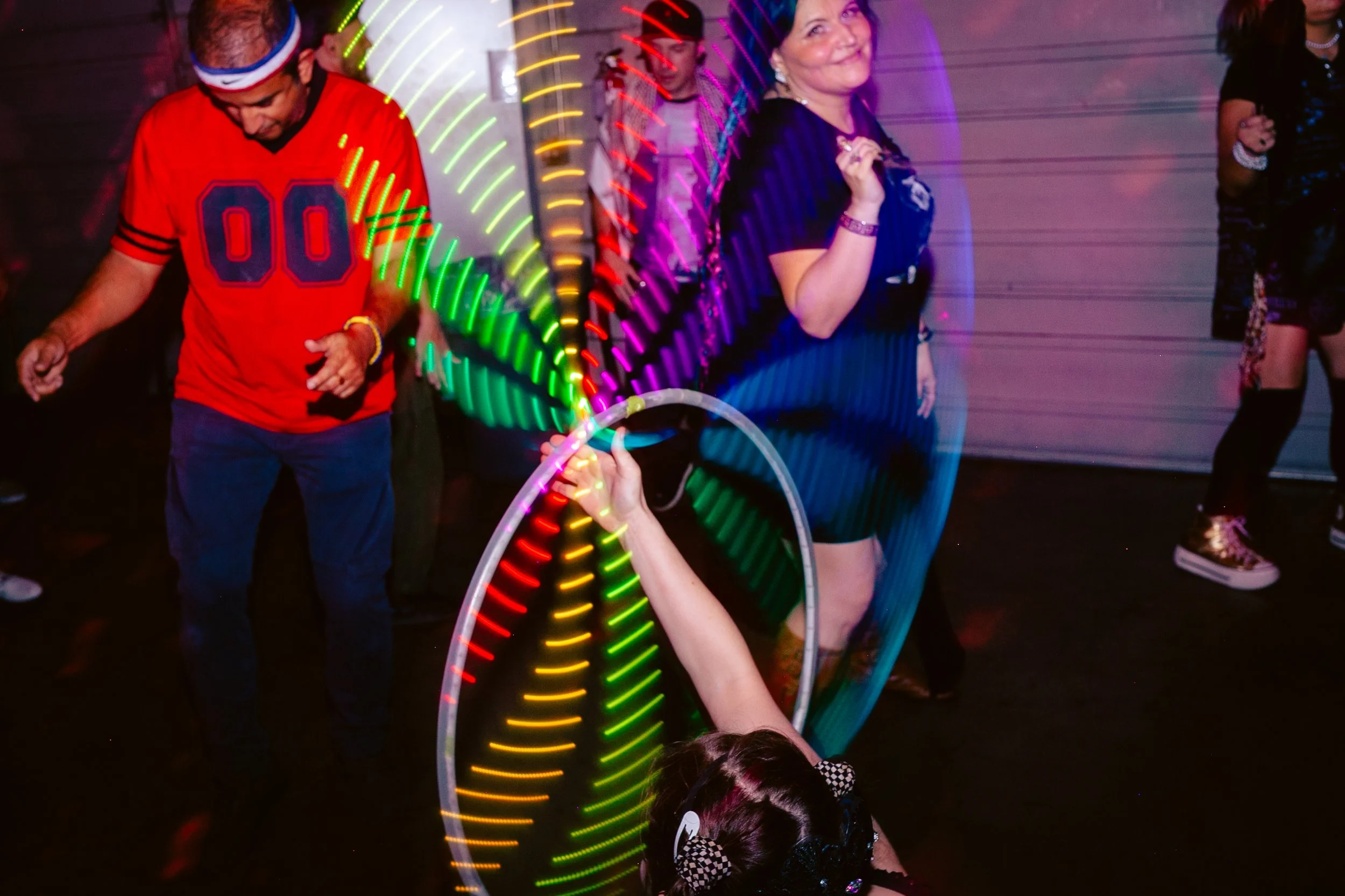 People dancing at a party with colorful light trails from glow sticks.