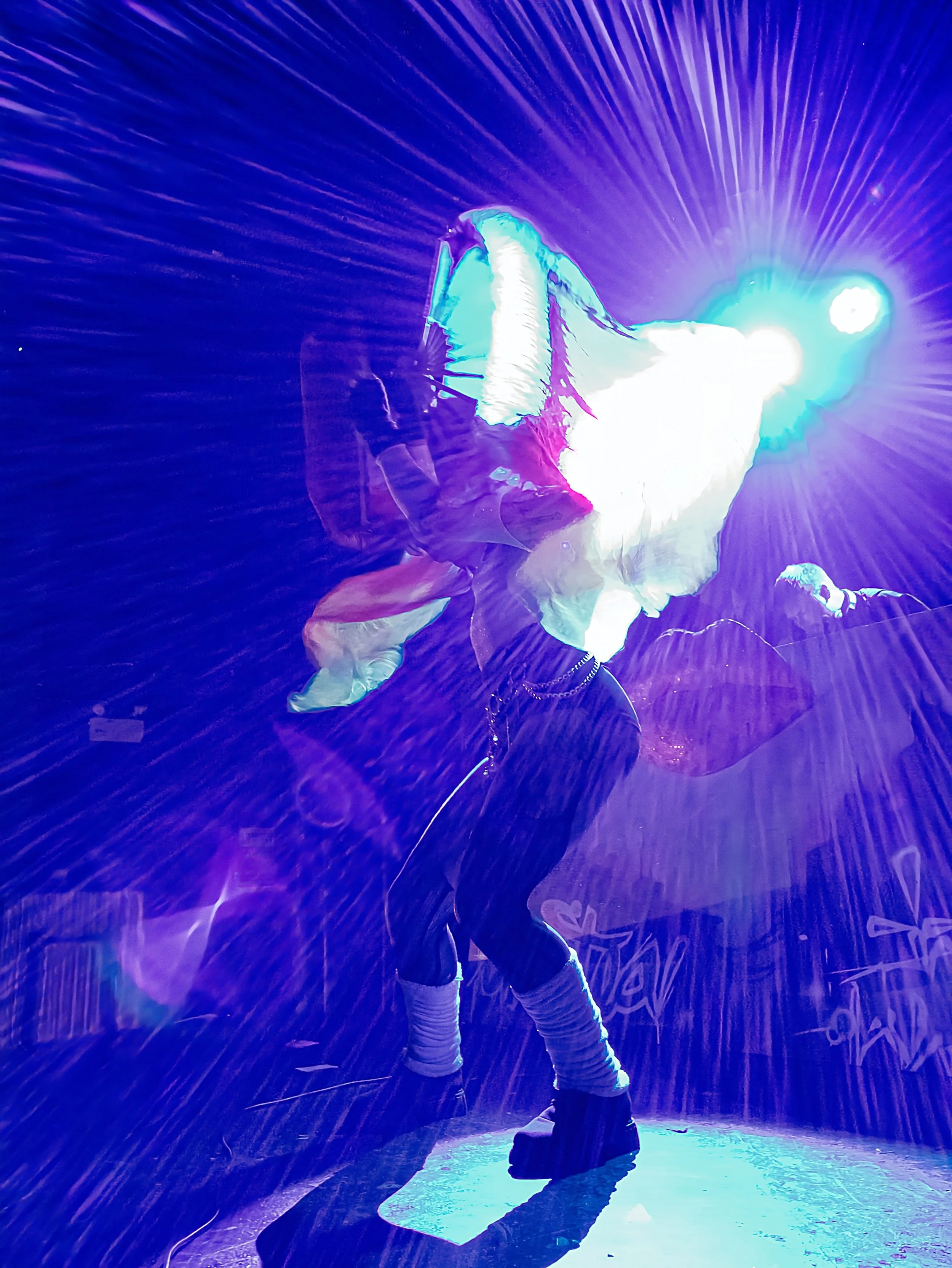A person is jumping into a pool at night under colorful, glowing blue and purple lighting.