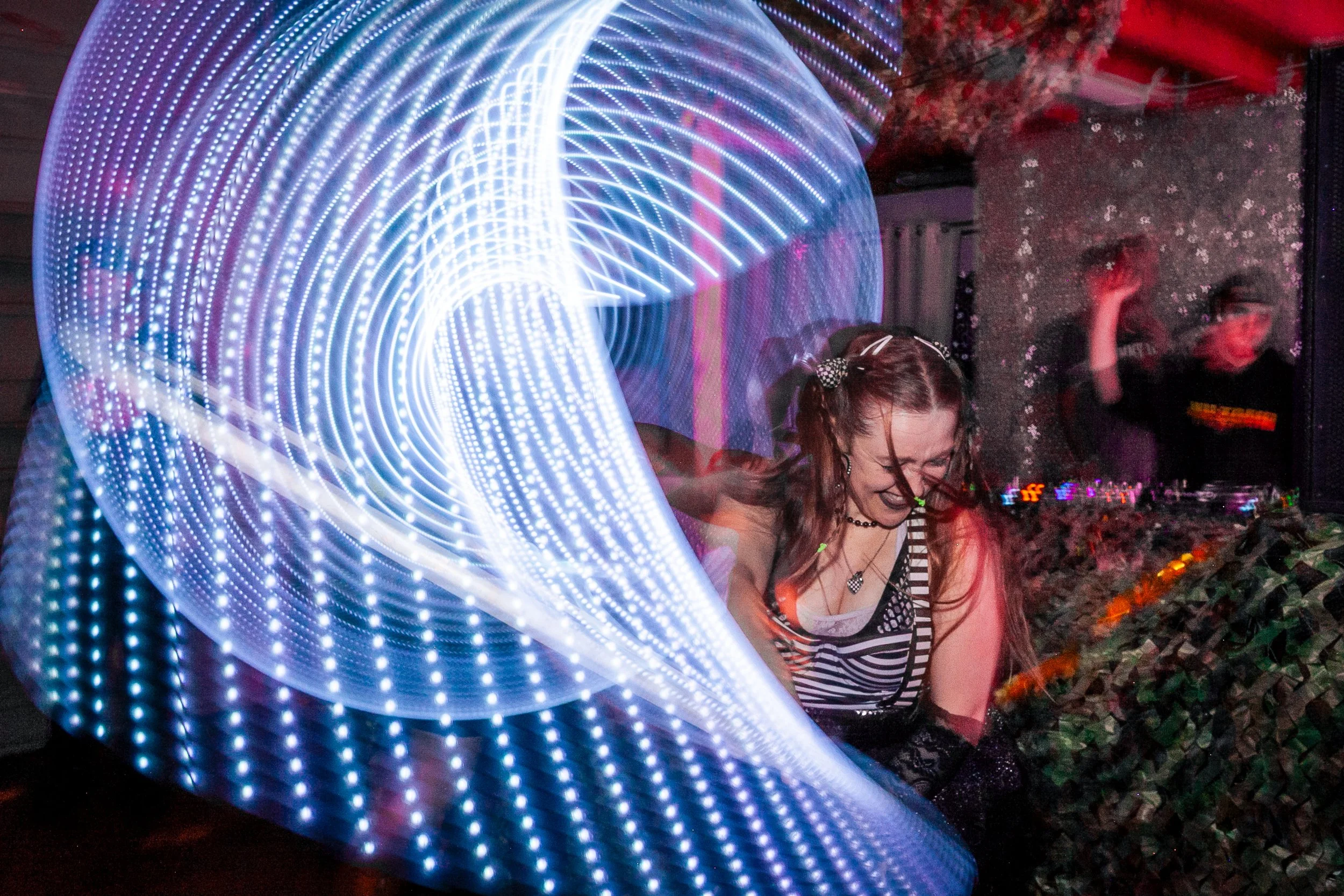 A person with glasses dancing at a party with colorful LED lights and patterned background.