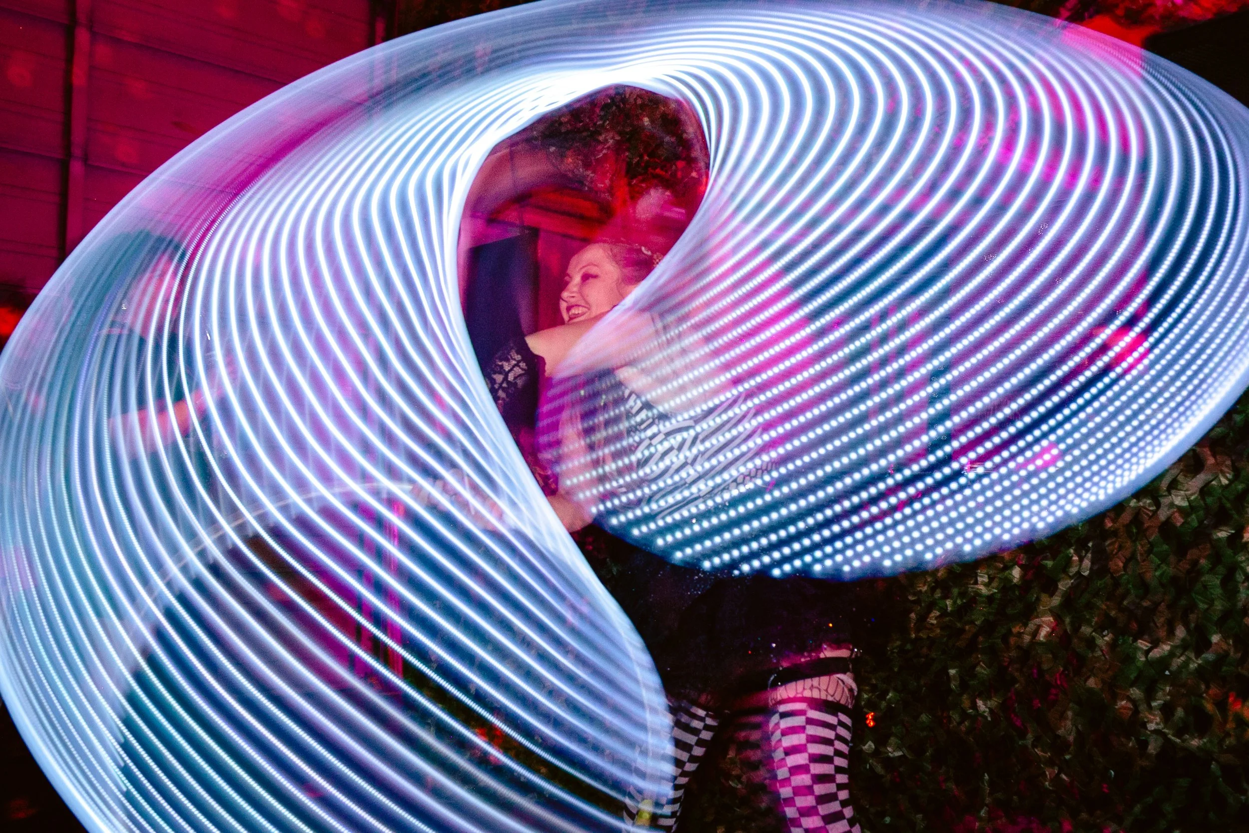 Two people embrace inside a swirling light tunnel at night, with one person's face showing a smile and wearing a black lace top, and the other person wearing checkered pants and shoes with a design.
