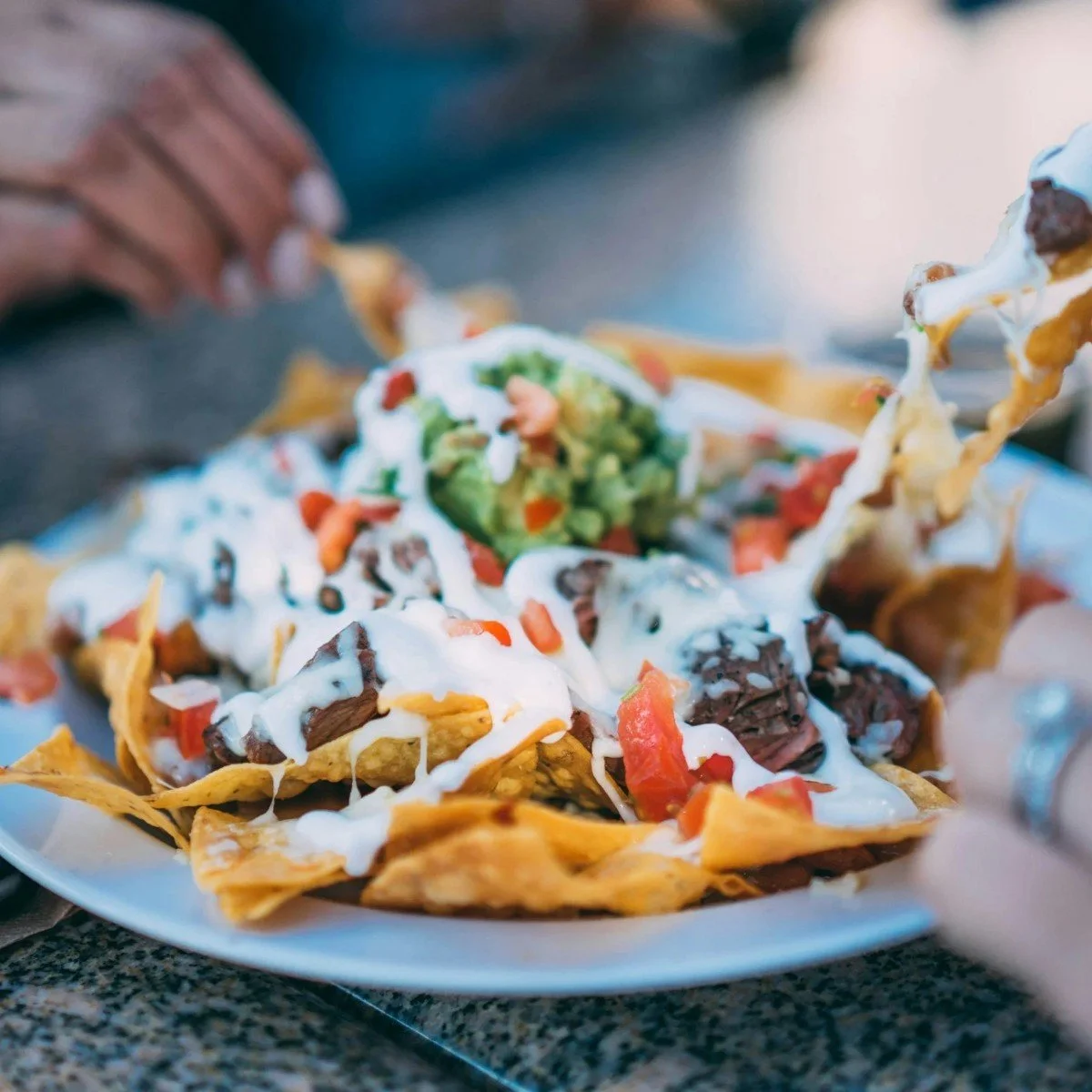 Plate of loaded nachos with melted cheese, diced tomatoes, guacamole, sour cream, and beef on crispy tortilla chips.
