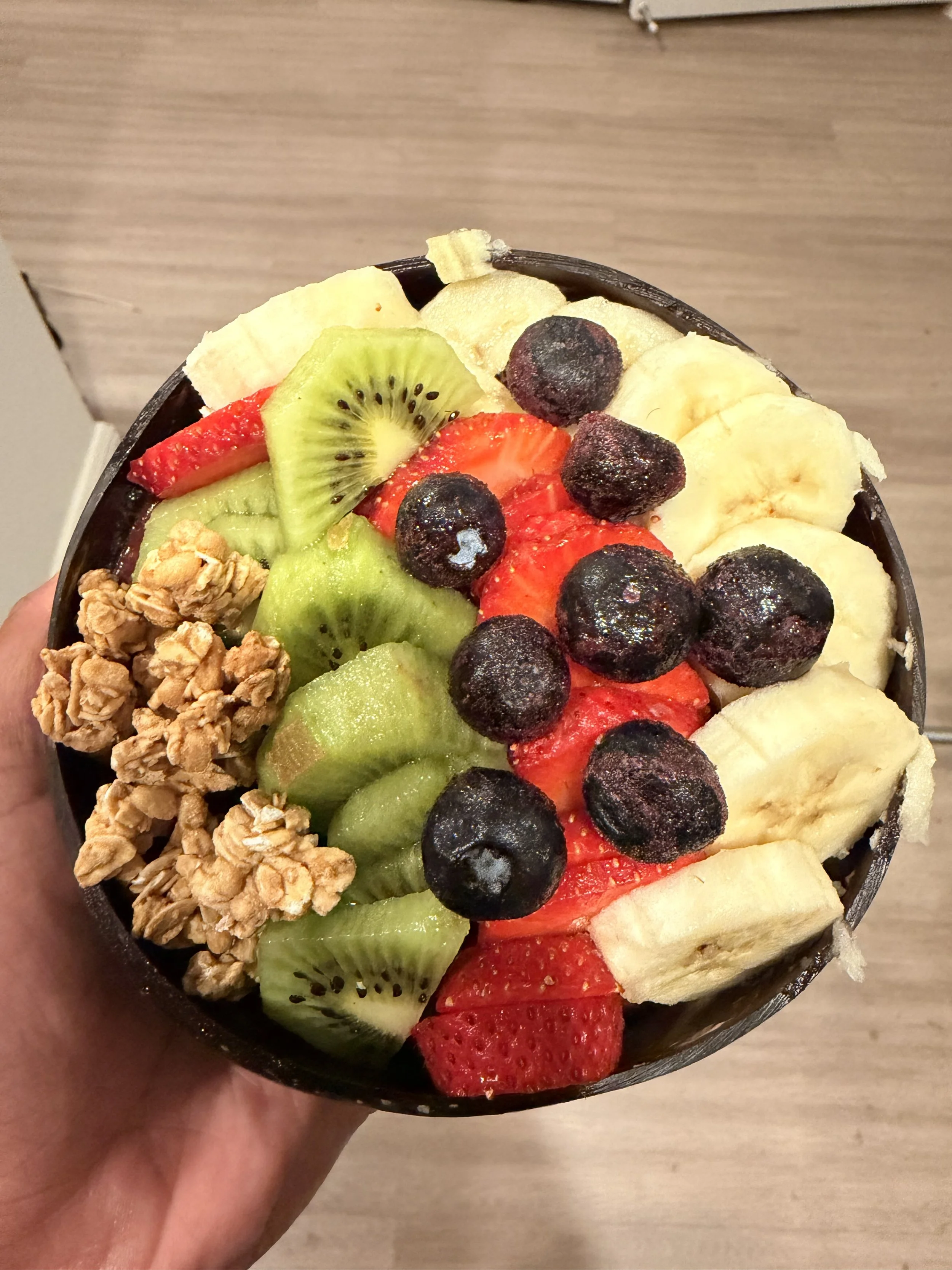 Close-up image of a bowl filled with various fresh sliced fruits including bananas, strawberries, kiwis, blueberries, and pineapples, with oat flakes on the side.