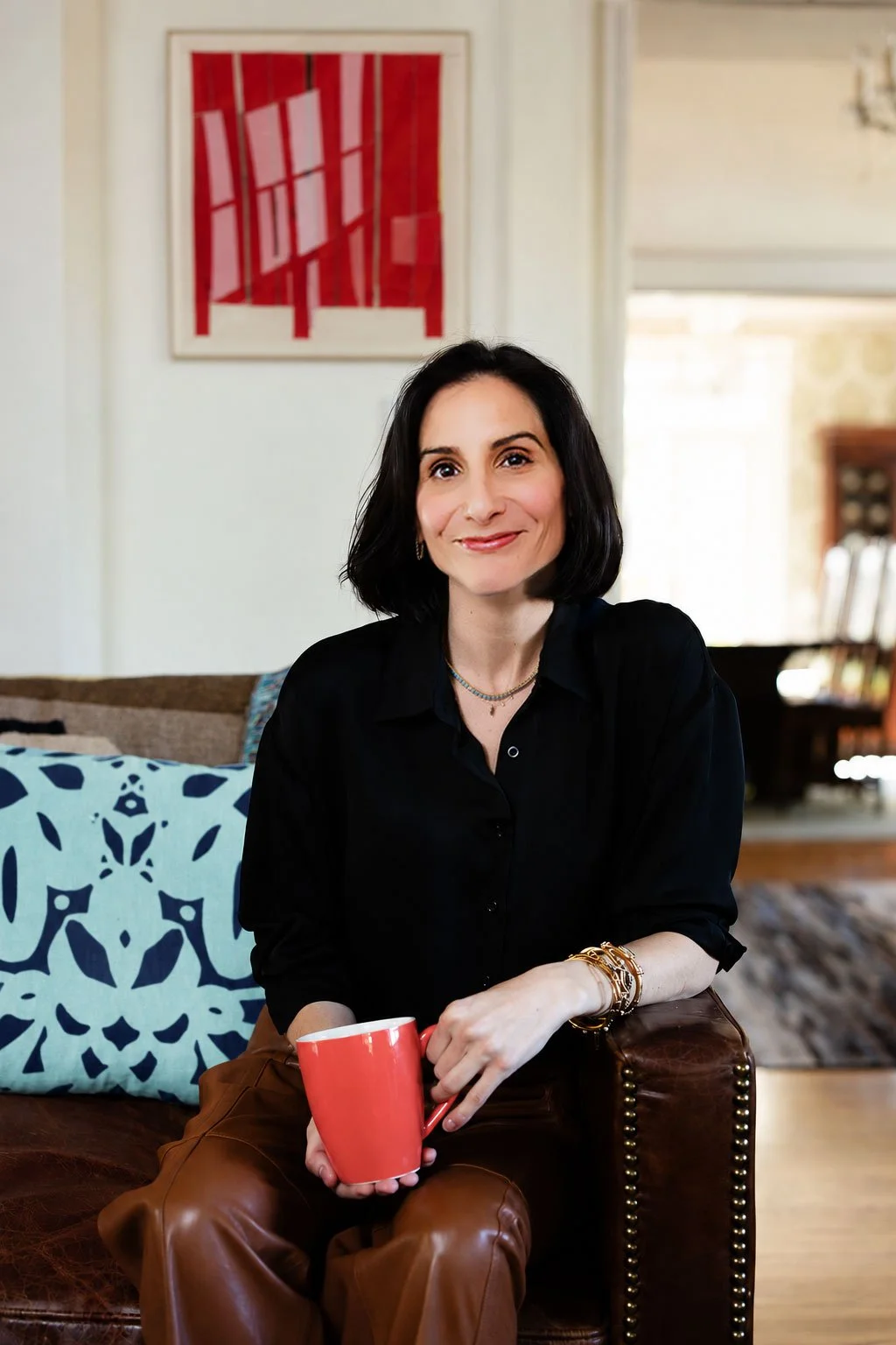 Whitney Light, CDFA, Certified Divorce Financial Analyst and Divorce Financial Strategist | Woman in a black blouse holding a red mug while seated in a leather chair at home