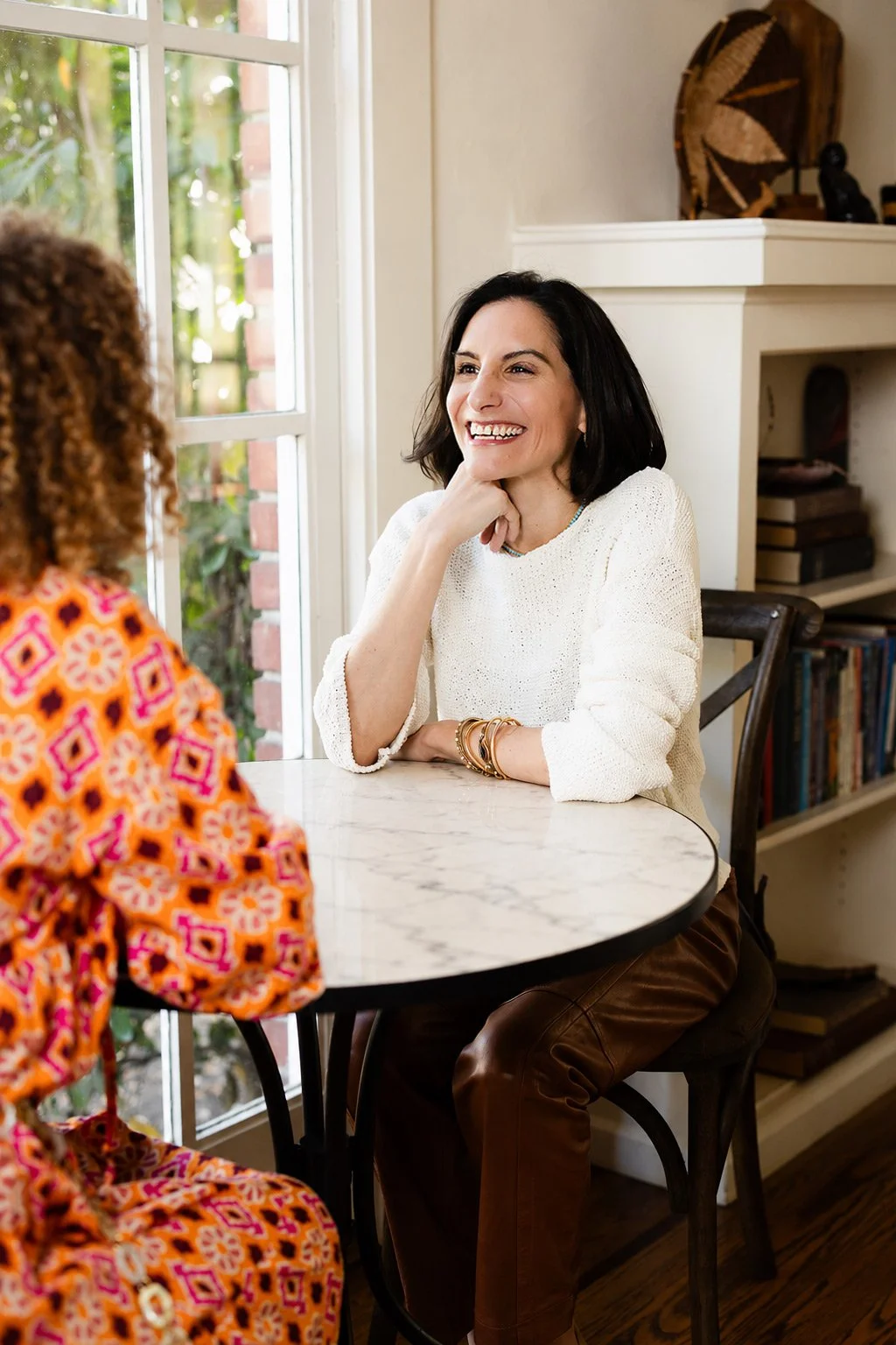 Whitney Light with a client | Two women smiling and talking at a round marble table in a bright living room.