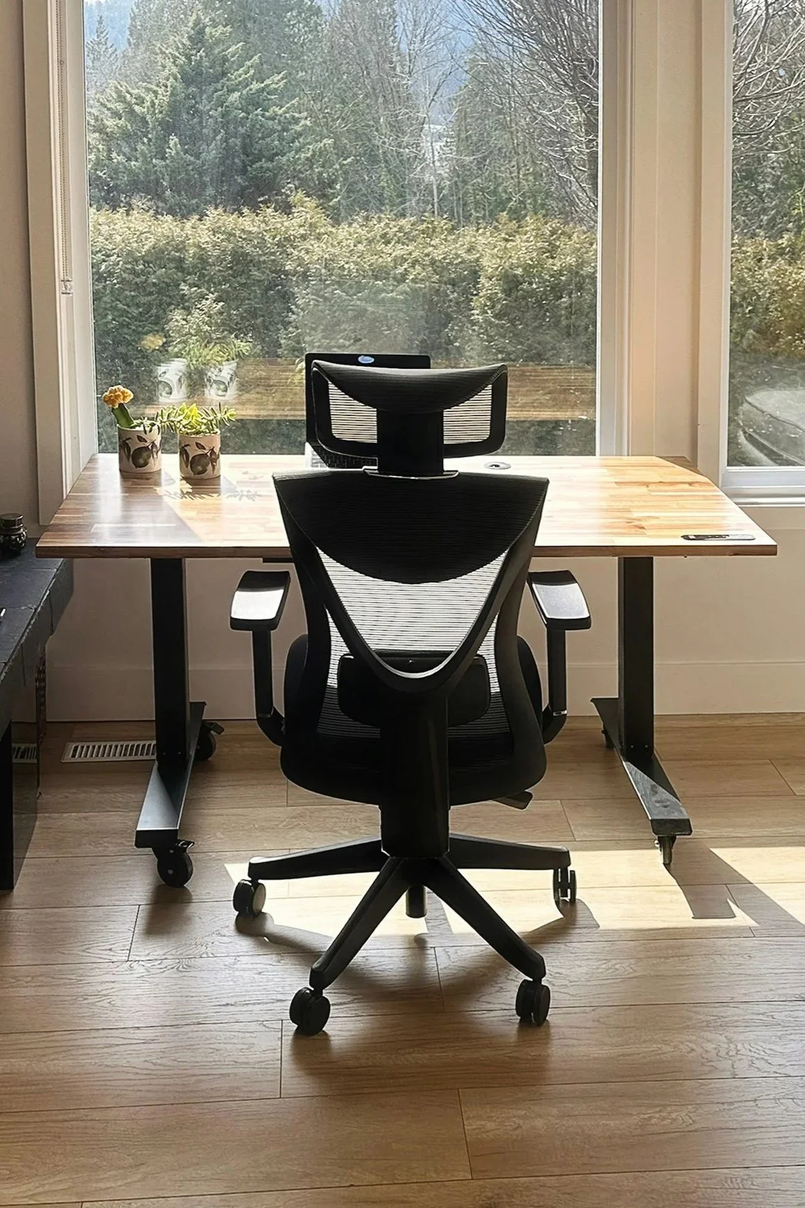 An ergonomic black office chair with a mesh back is positioned in front of the desk.