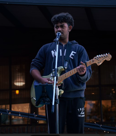 Young man singing into a microphone while playing an electric guitar.