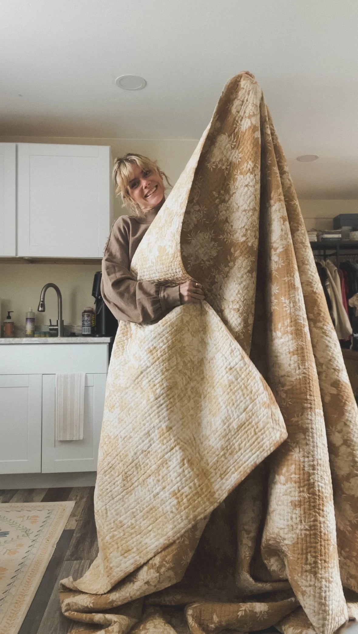 Alicia holding up a large vintage quilt with intricate stitching and a neutral floral design, preparing to transform it into handmade clothing.