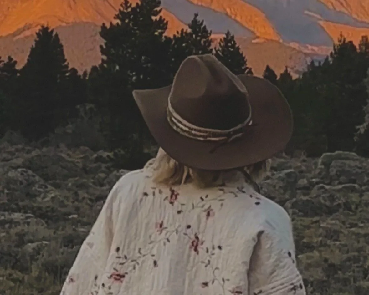 Woman wearing a cowgirl hat and vintage-inspired floral quilt jacket in the Colorado mountains at sunset