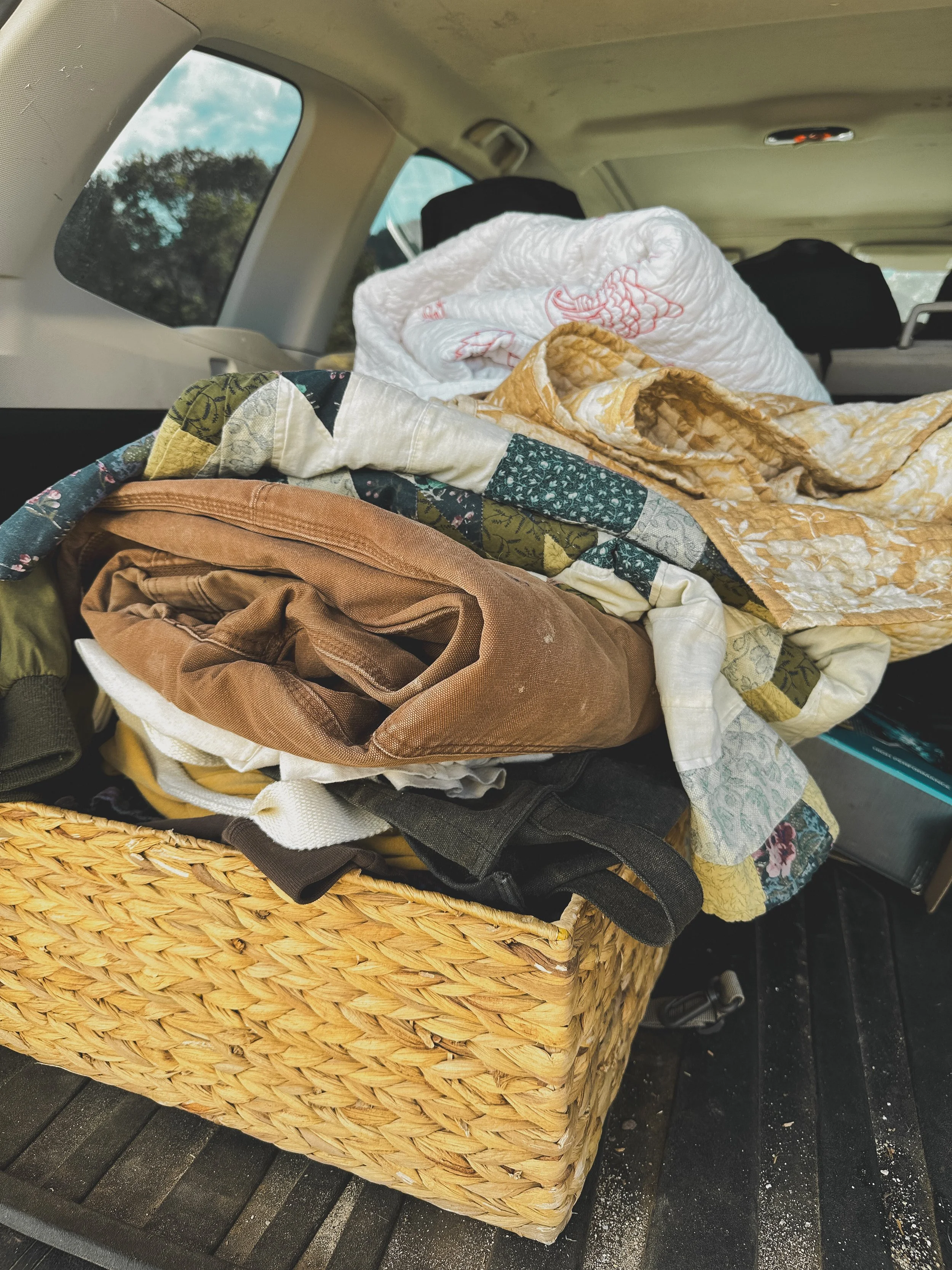 A wicker basket filled with colorful vintage quilts and fabrics, collected to be transformed into one-of-a-kind handmade creations by Xo alicia jo.