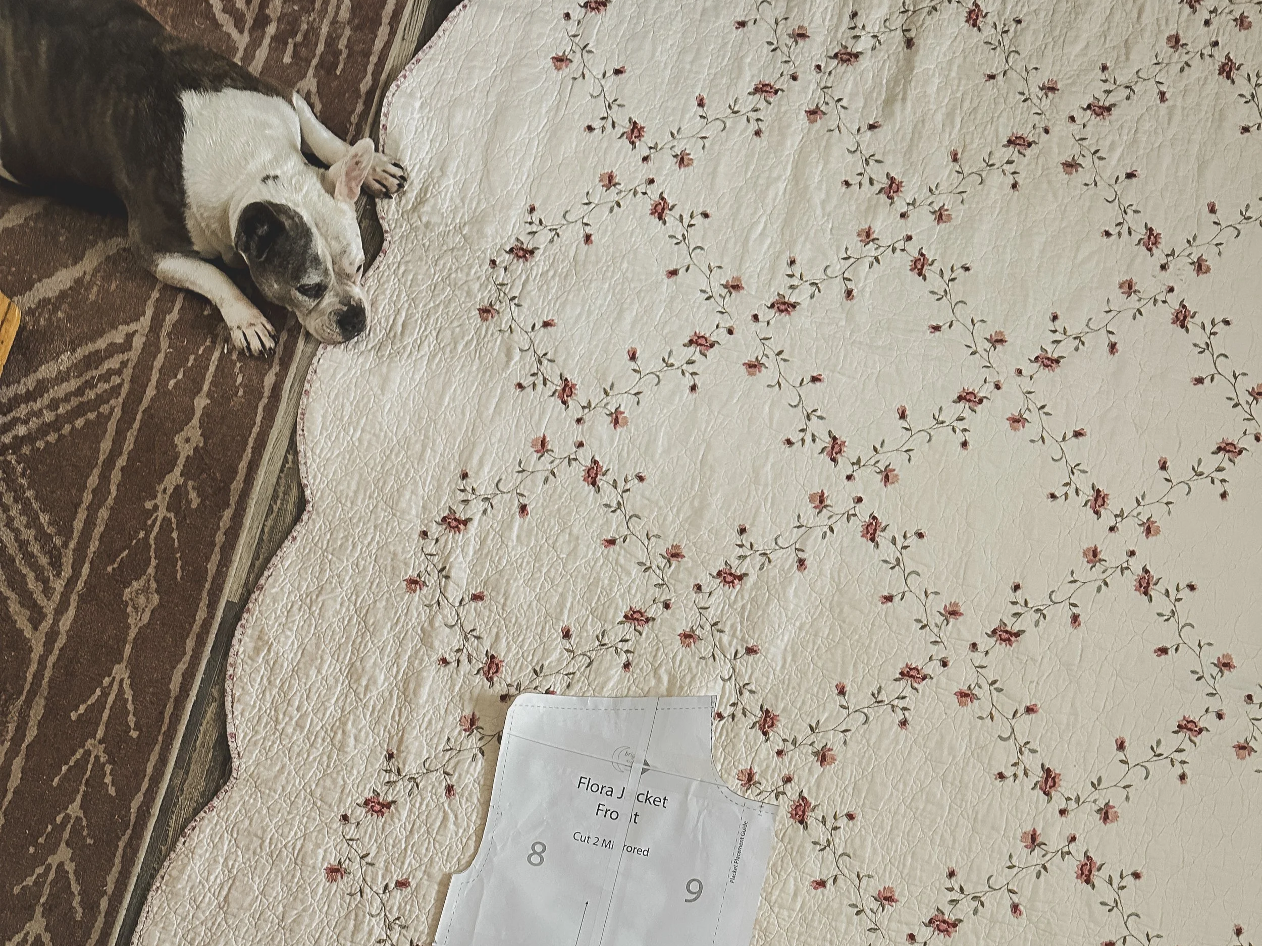 A white fabric with a floral pattern of pink and red flowers and green leaves, laid flat on a surface, with a piece of paper containing printed text partially visible at the bottom.