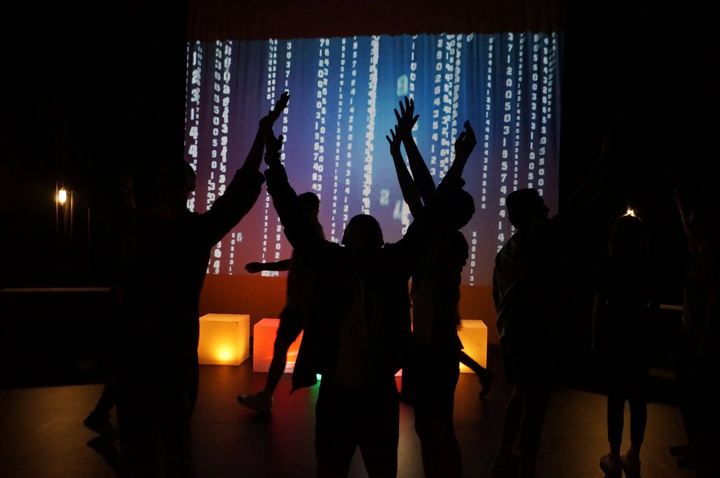 Silhouetted people dancing with raised hands in front of colorful digital number projections