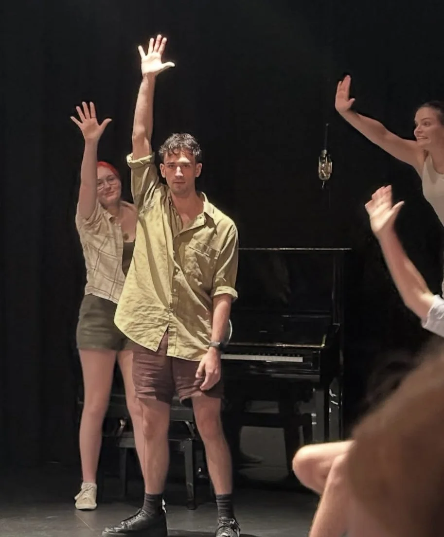Four performers raise their hands onstage in front of a piano during a theater performance.