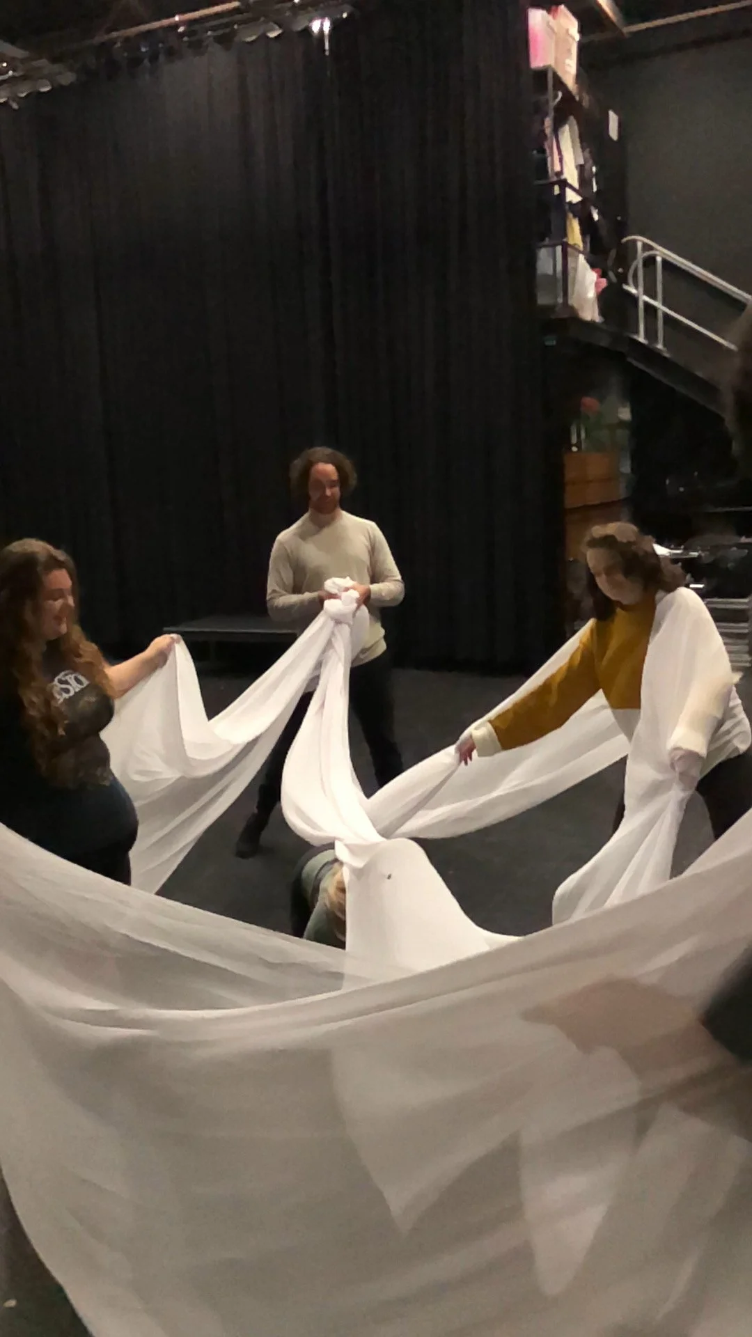 People rehearse a theater performance using large white fabric on a stage.