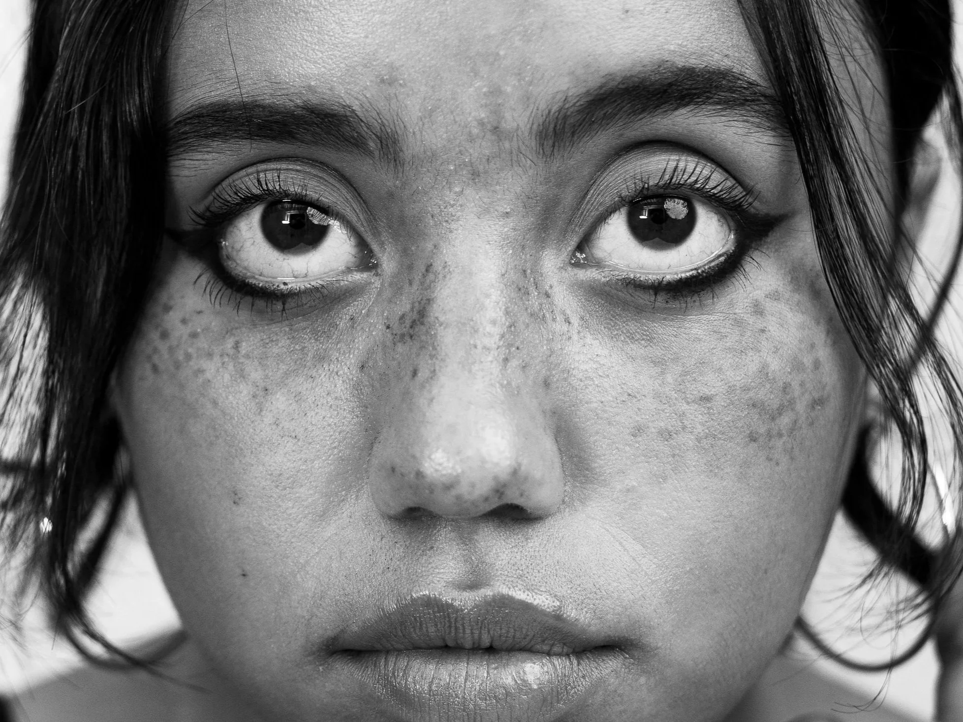 Close-up of a woman's face in black and white, focusing on her eyes and nose, with wet curly hair framing her face.